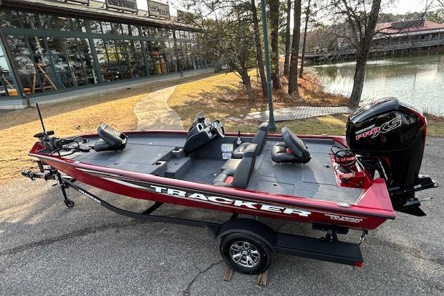 2025 Tracker Pro Team 190 boat, red, parked near a lake with trees in the background.