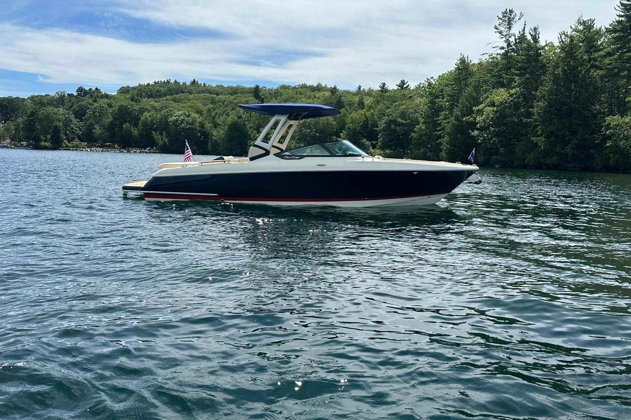 2026 Chris-Craft Sportster 28 boat on a serene lake with lush green trees.