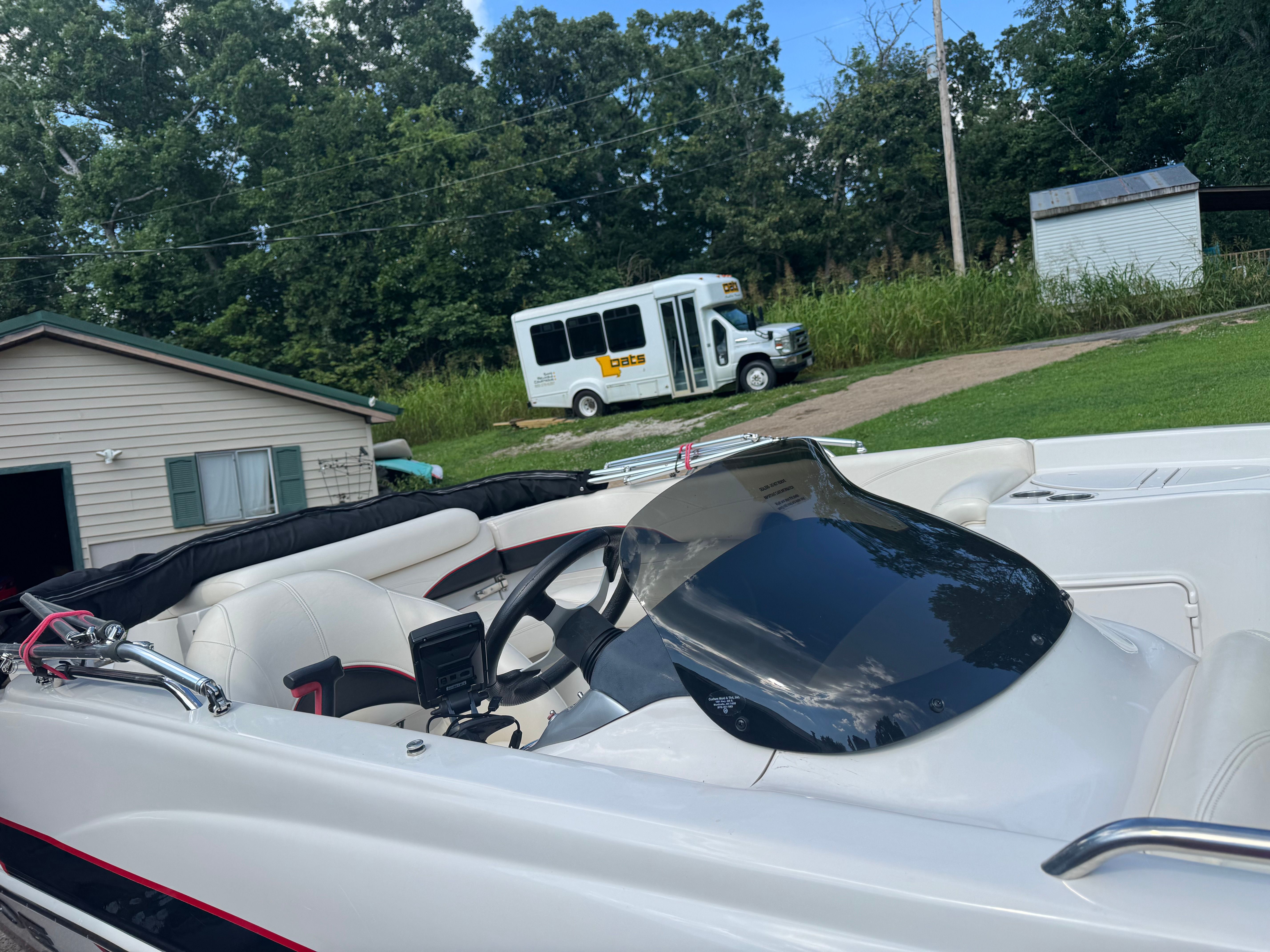 A white boat with a black windshield is in a green yard. A bus is in the background.