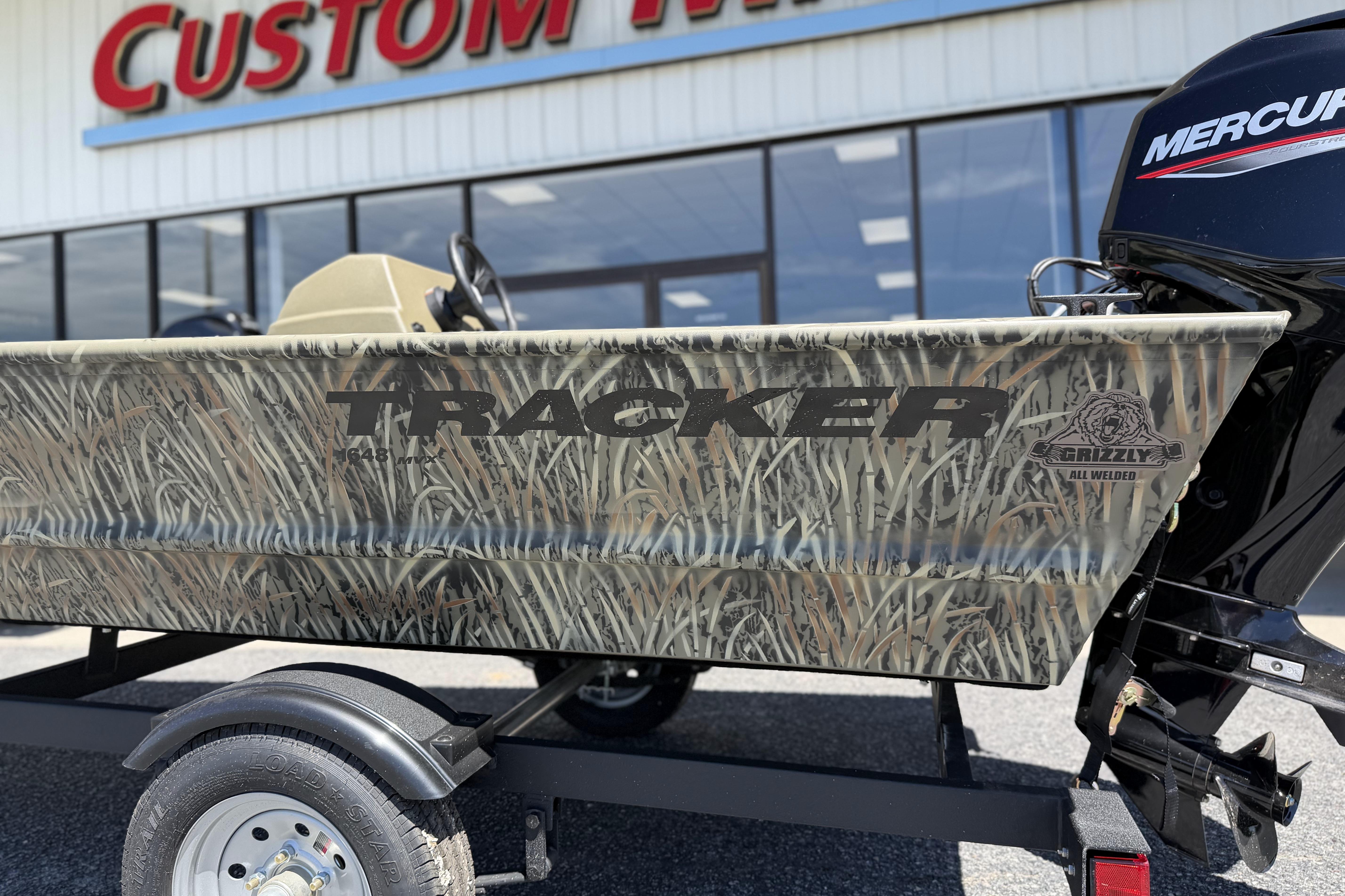 2026 Tracker Grizzly 1648 SC boat with camouflage design, parked outside a custom marine shop.