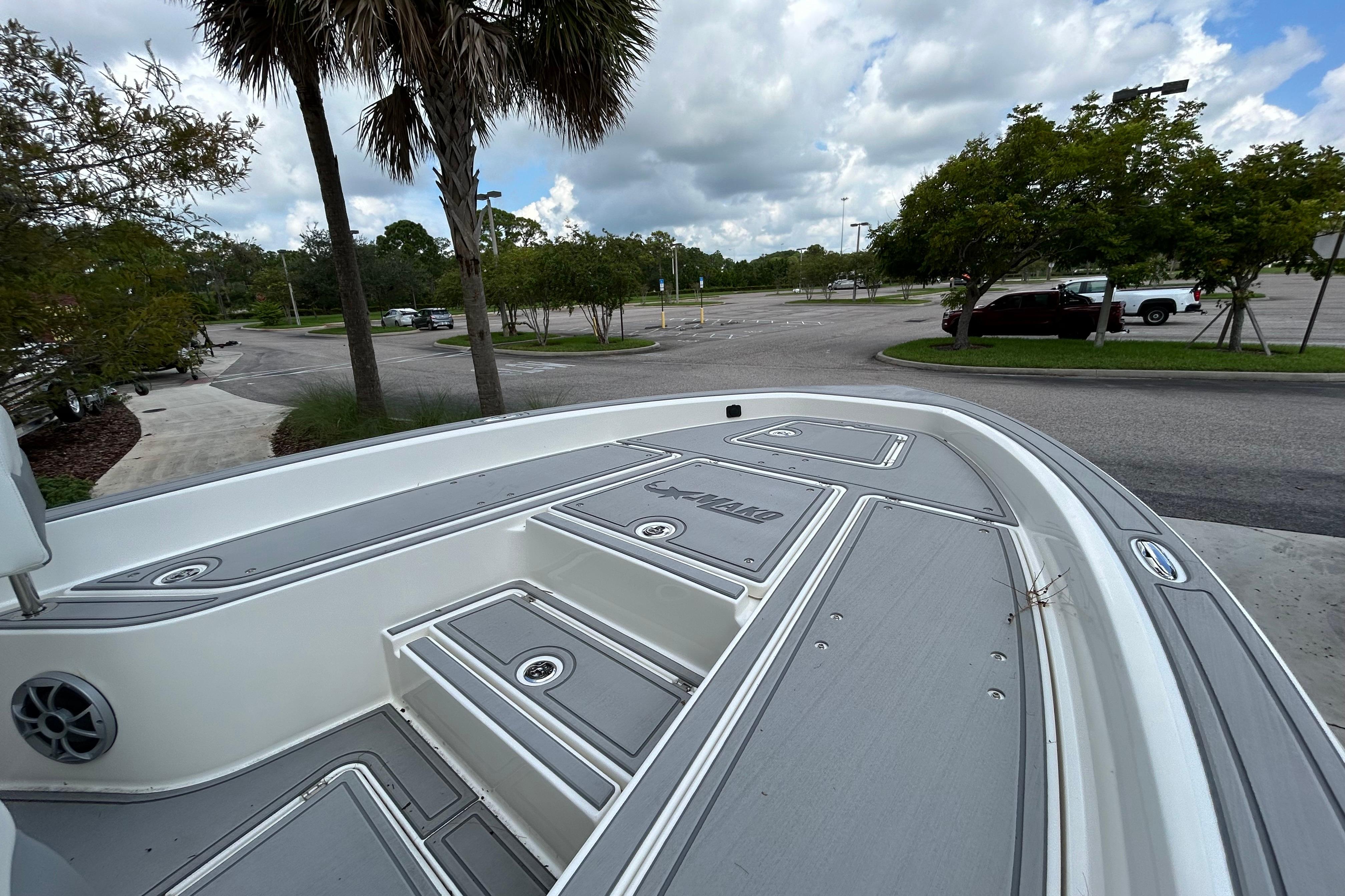 2025 Mako 24 APEX boat deck in a parking lot, surrounded by trees and cloudy sky.