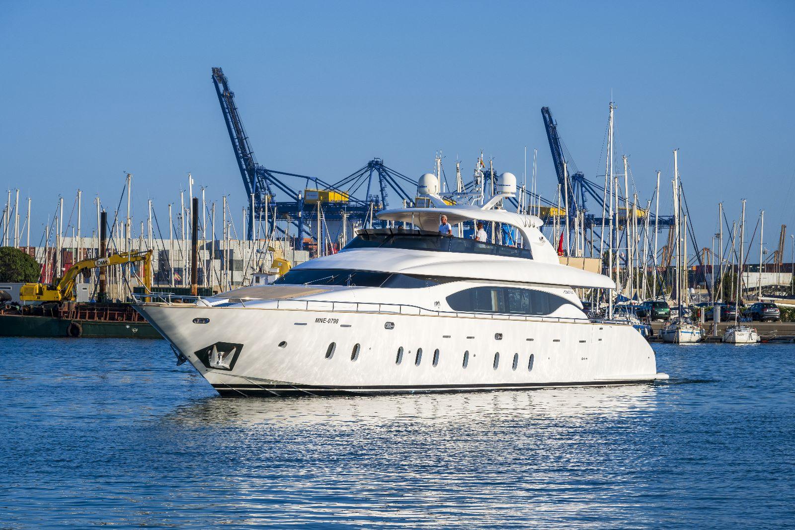 Luxurious 2011 Maiora 27 yacht cruising in a bustling marina with cranes and sailboats.