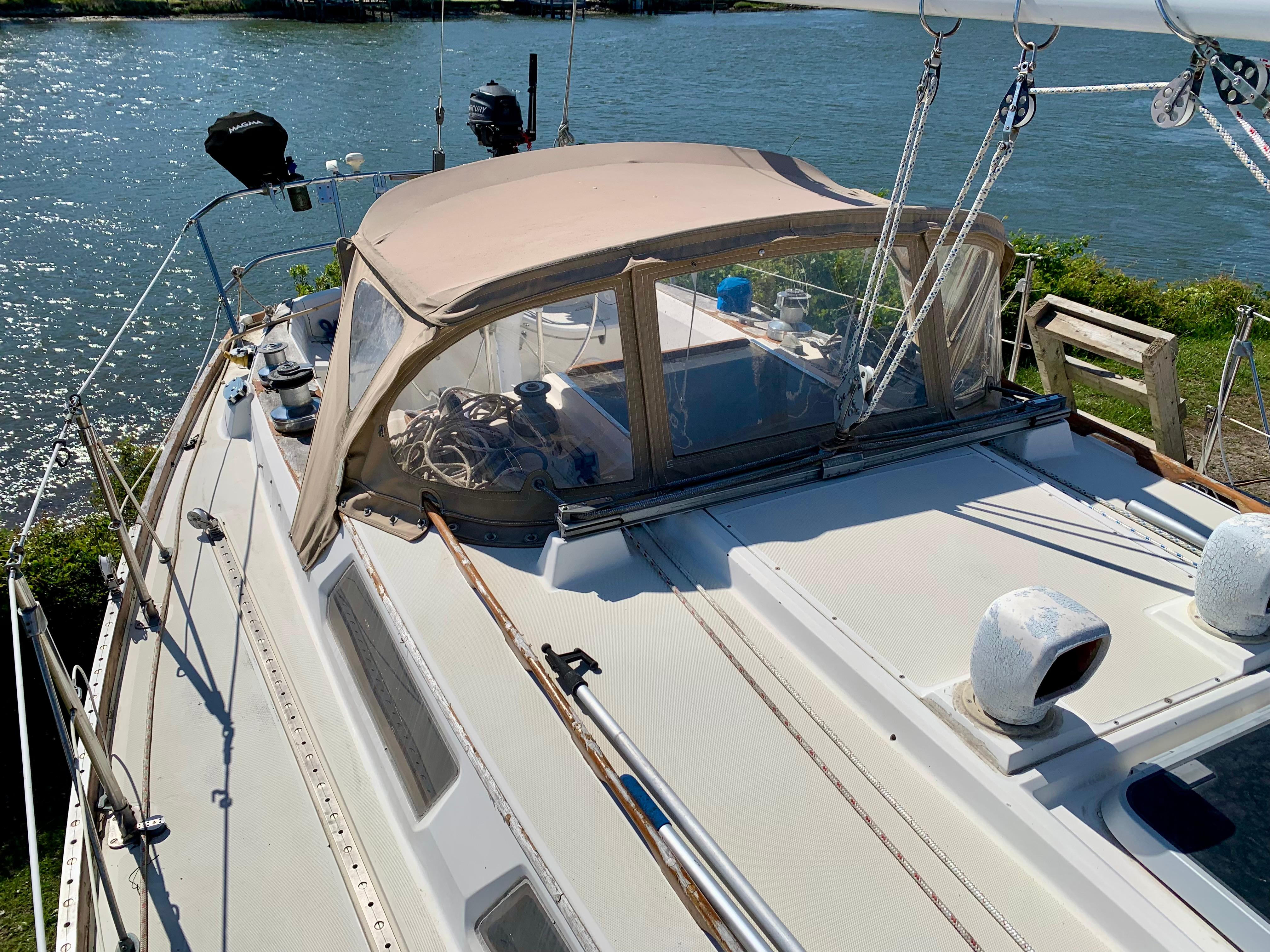 1986 Sabre 36 sailboat with beige canopy, docked by a scenic waterfront.