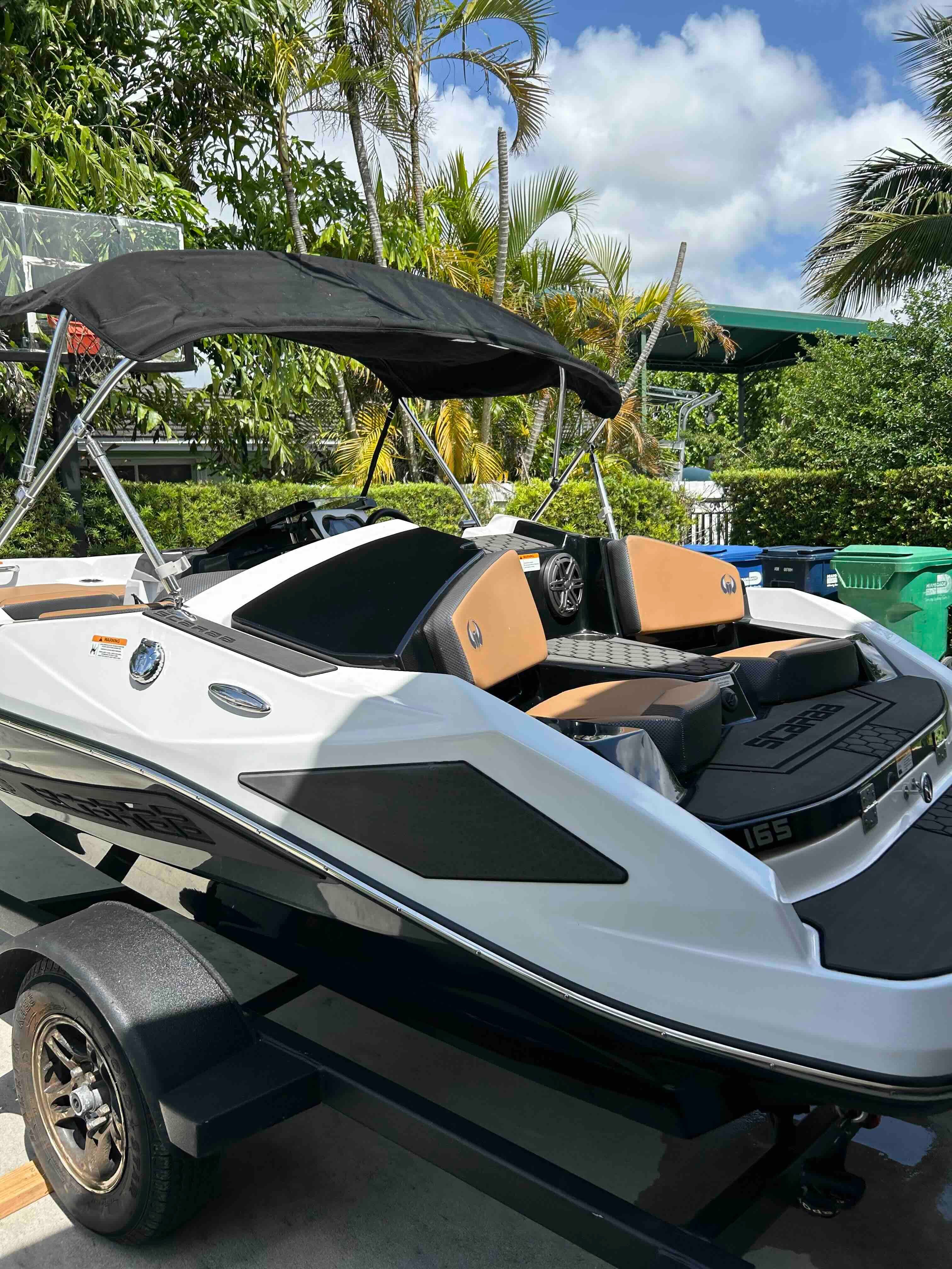 A 2022 Scarab 165 ID boat on a trailer, surrounded by tropical plants.