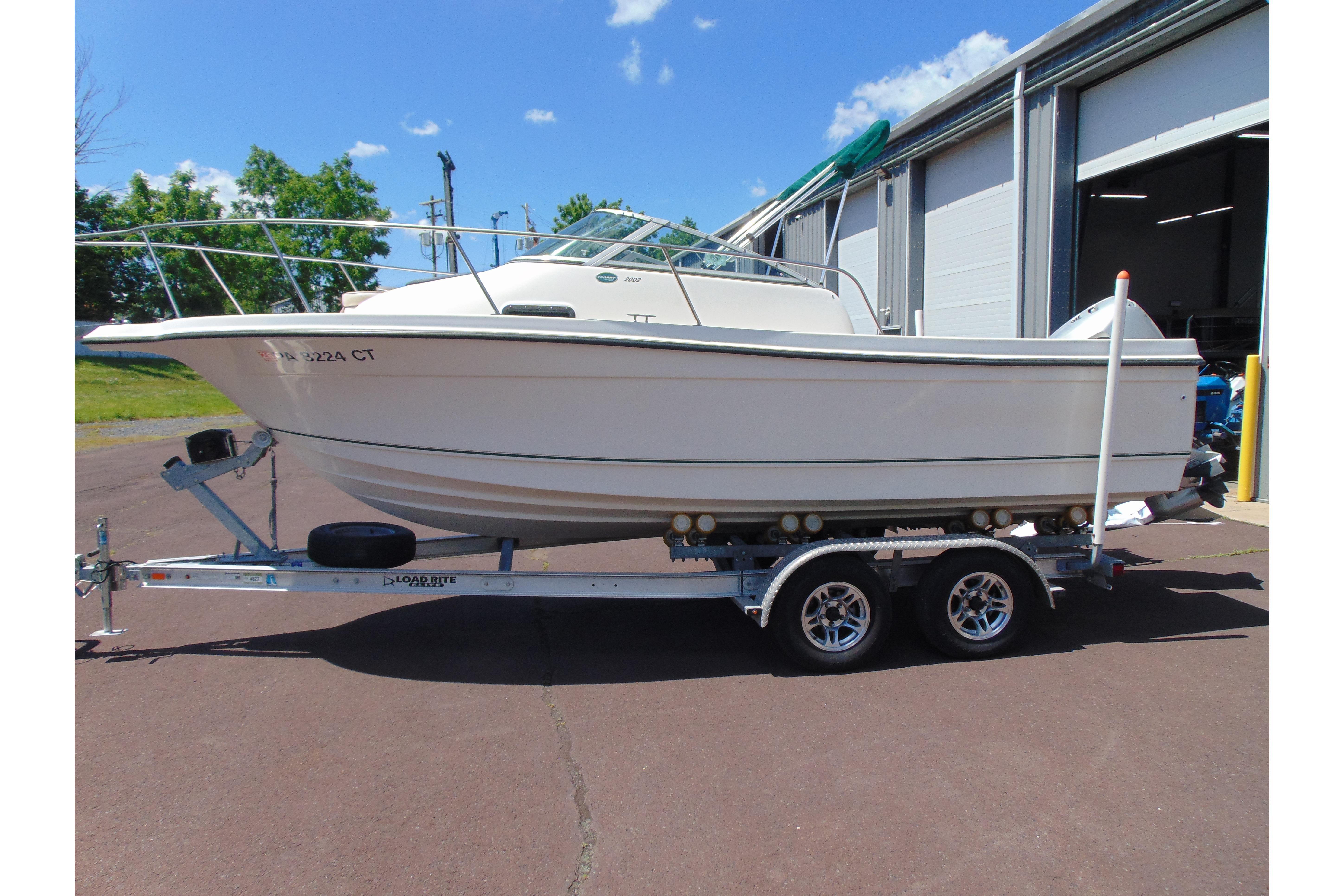 2002 Trophy Walkaround boat on trailer, parked outside a garage under a clear blue sky.