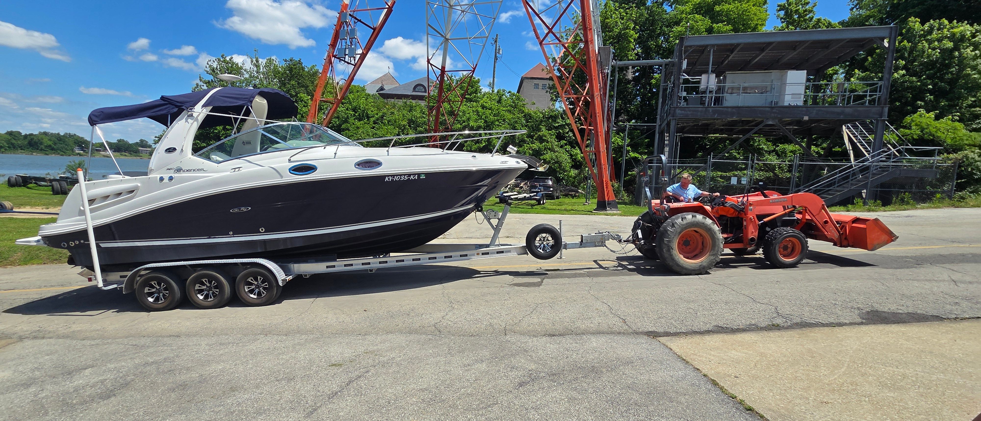 A 2005 Sea Ray Sundancer 260 is being towed on a trailer by a tractor.