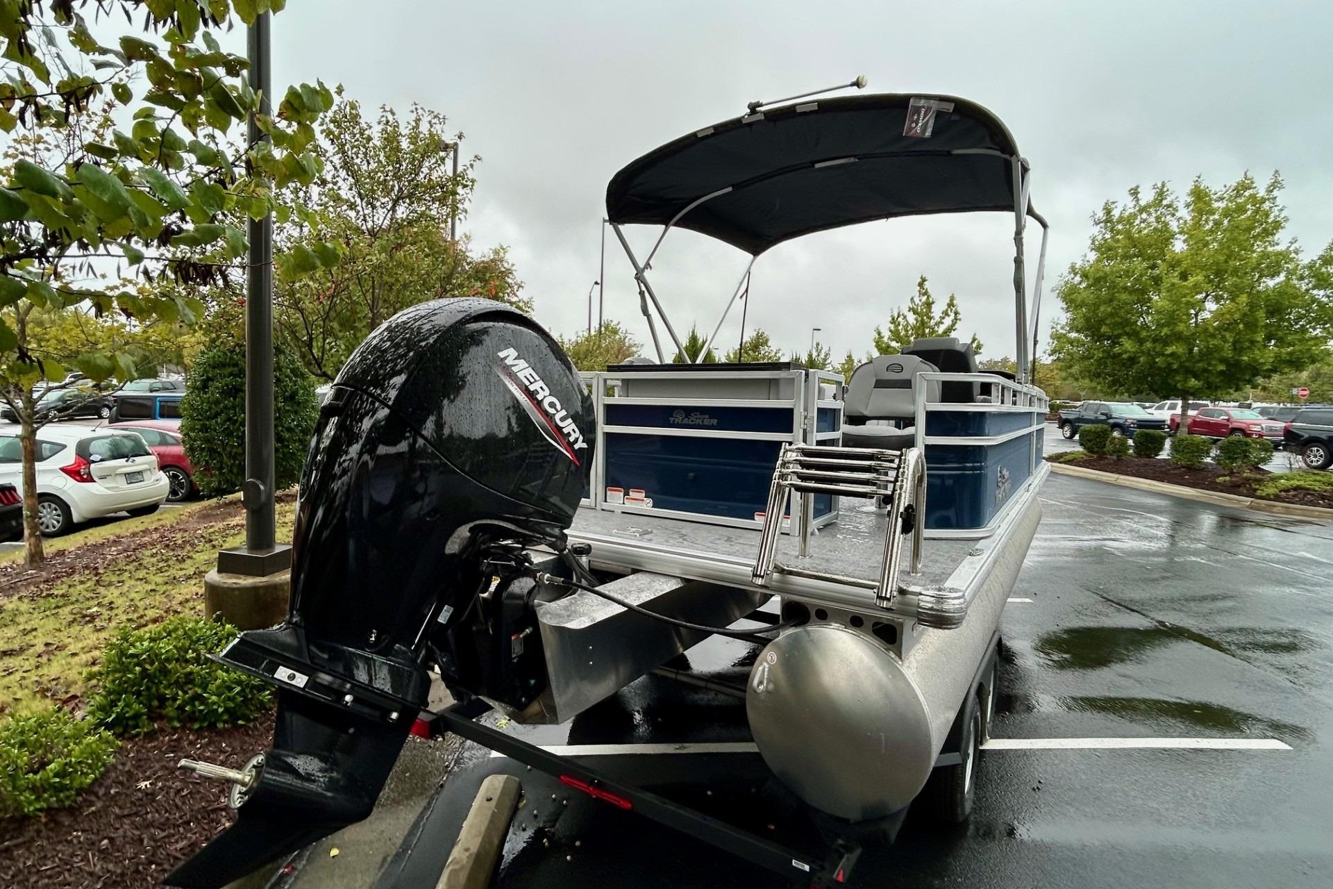2026 Sun Tracker SportFish 22 DLX pontoon boat with Mercury outboard motor in parking lot.