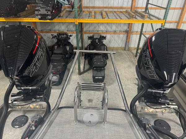 2025 Manitou LX boat with dual outboard motors in a storage facility.