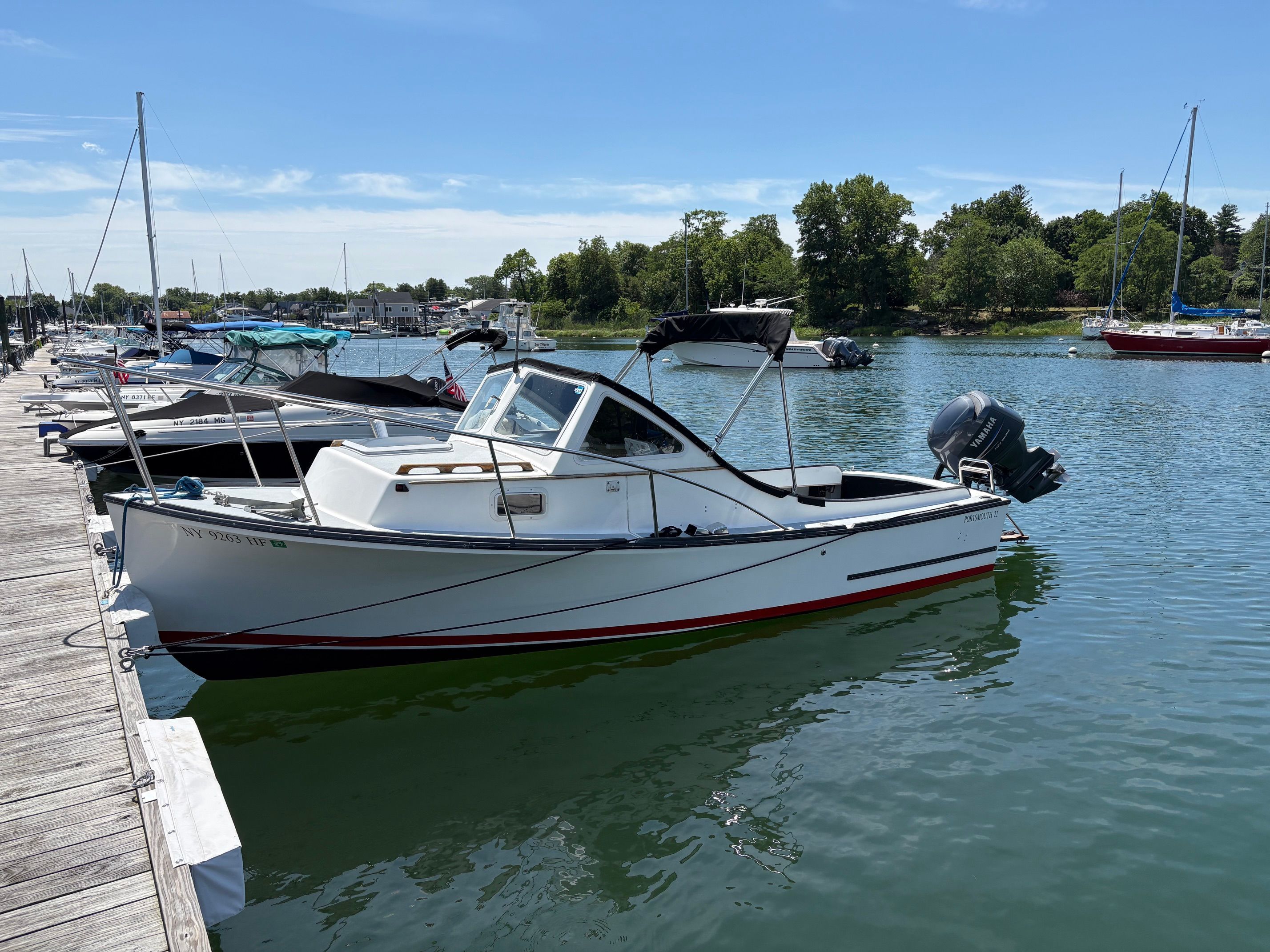 A white 1990 Portsmouth 22 boat docked on a sunny day, surrounded by other boats.