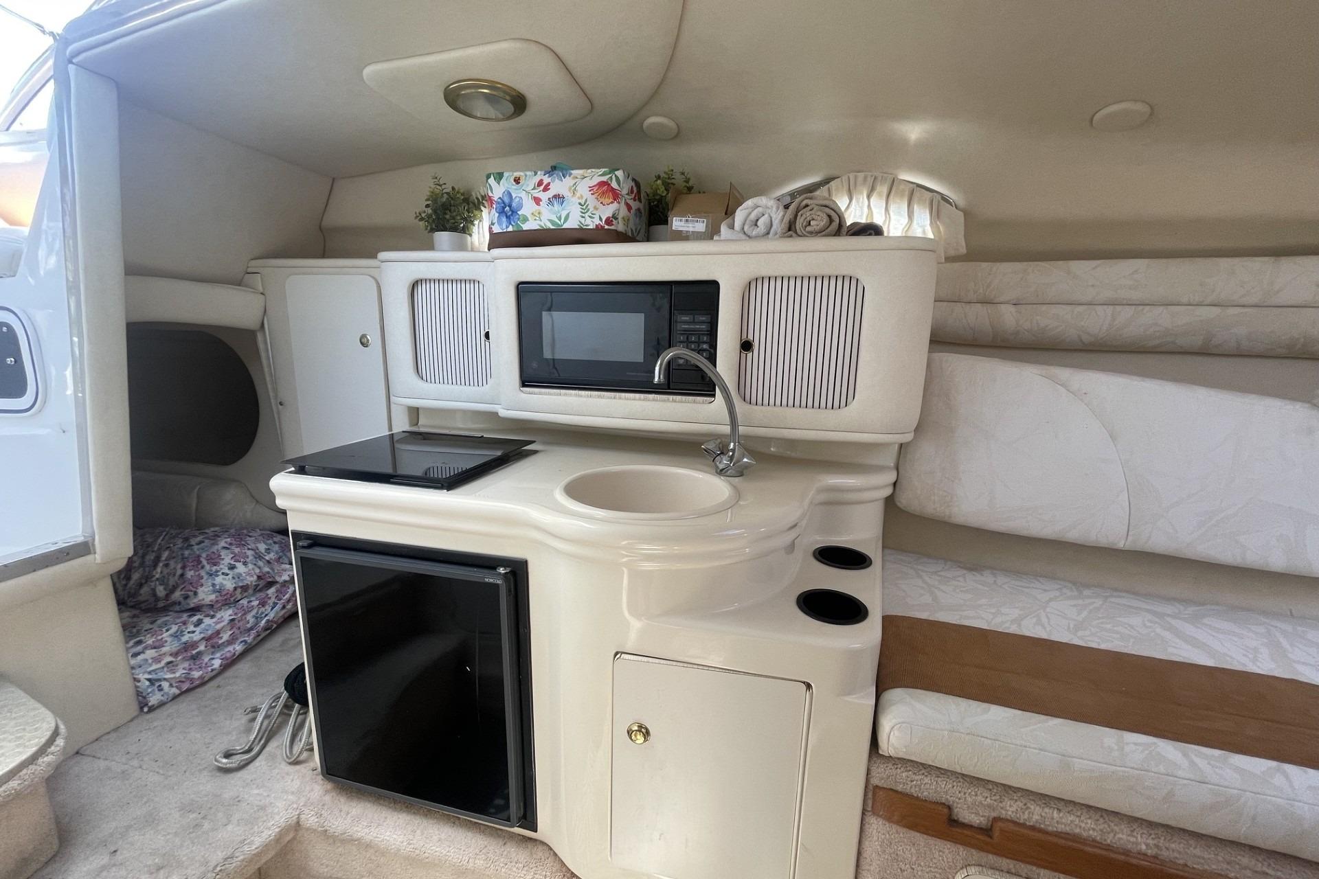 Interior of 2000 Sea Ray Sundancer 260, featuring kitchenette with sink, microwave, and compact fridge.