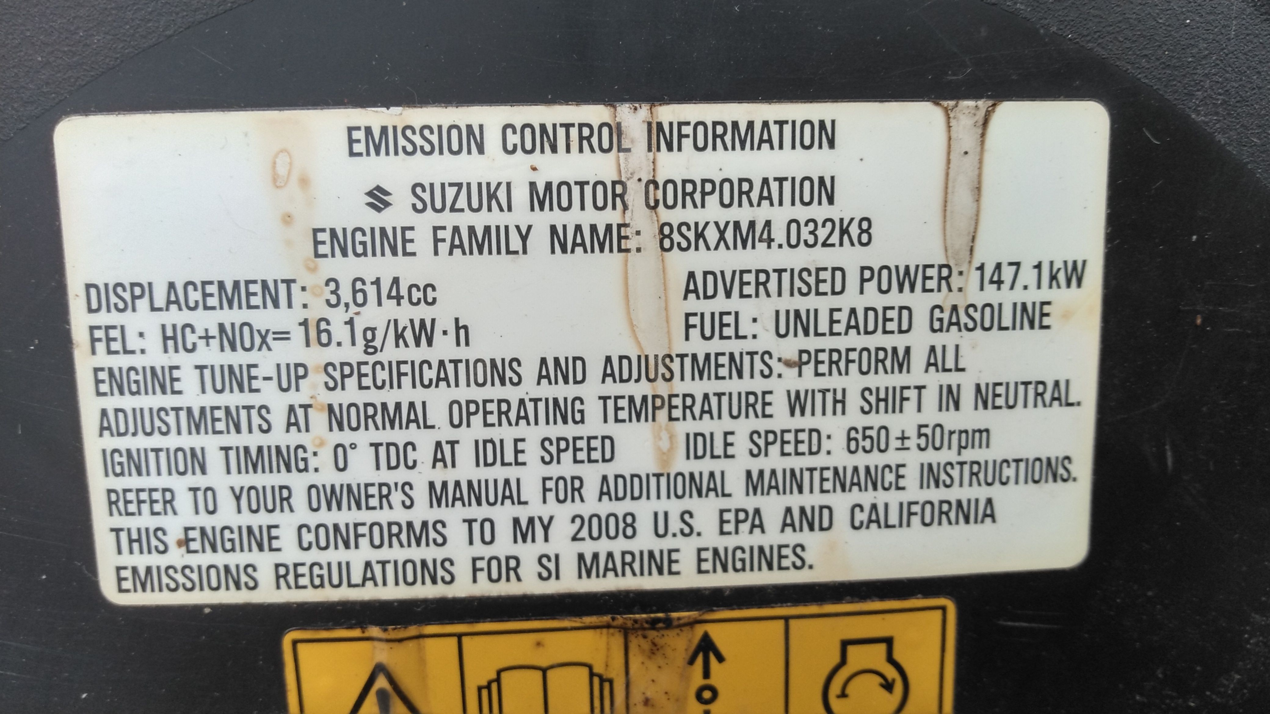 An emission control label with technical details of a Suzuki engine.