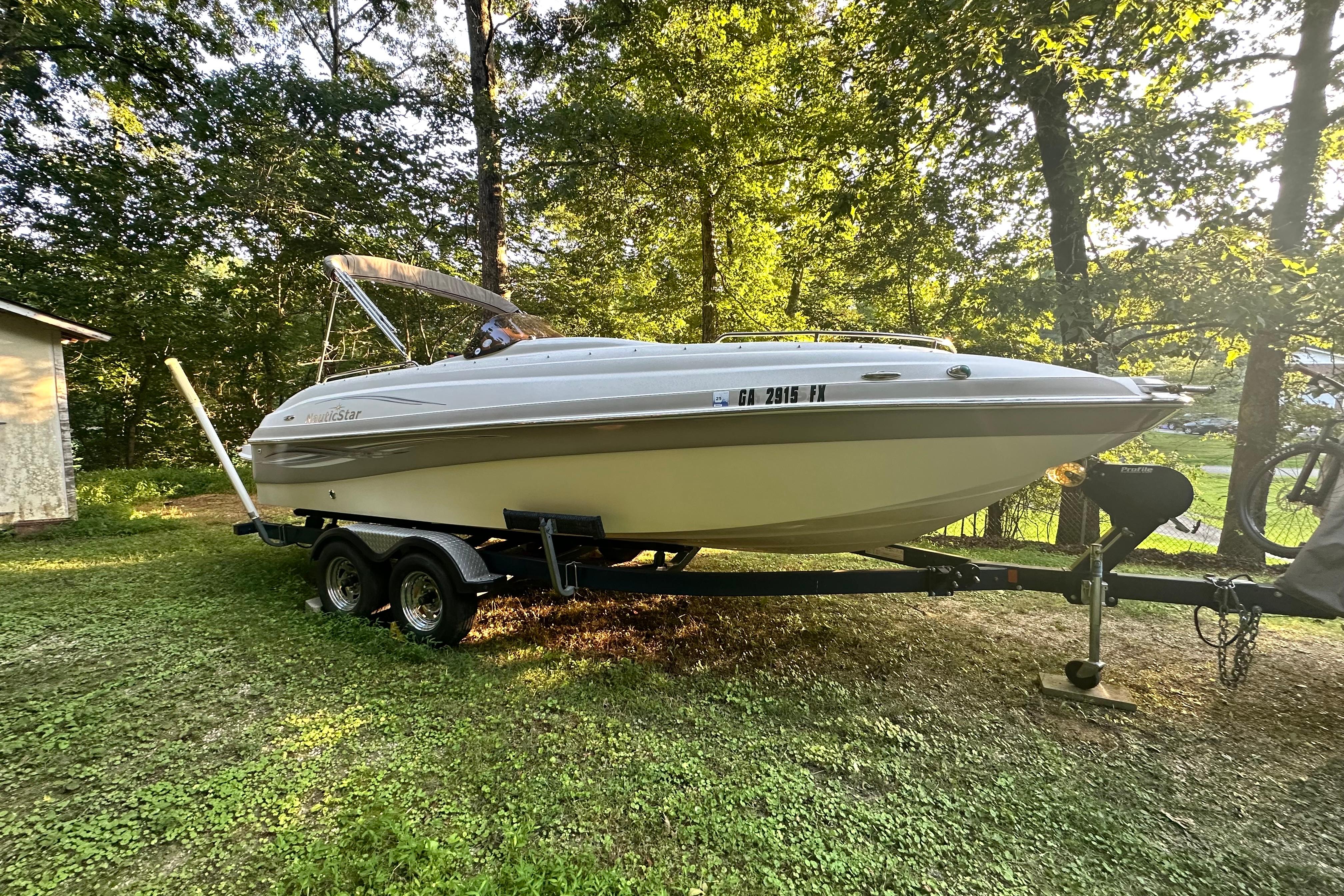 2008 NauticStar 230 SL Sport Deck I/O boat on trailer in wooded area.