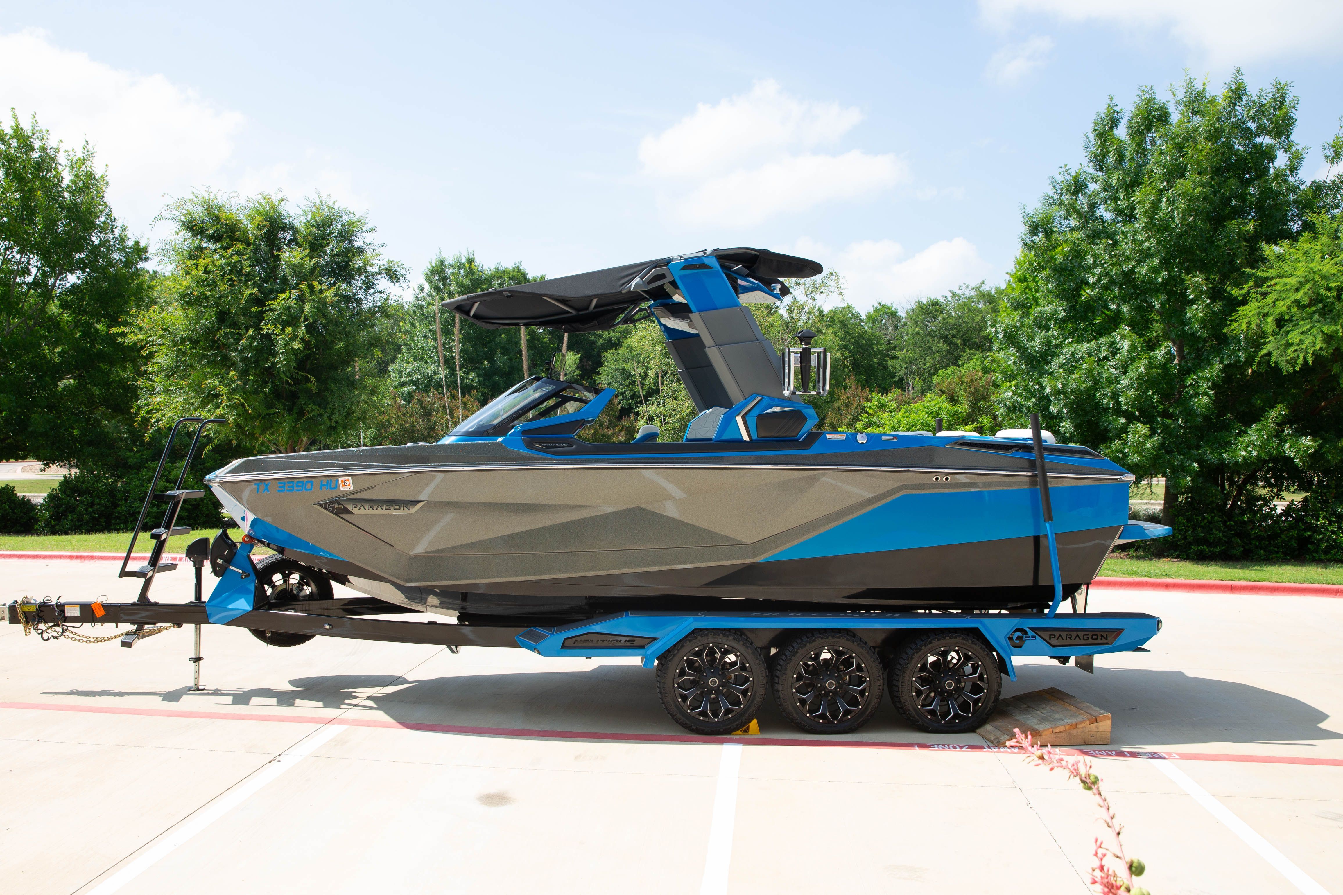 A blue and gray boat on a trailer, surrounded by trees and a sunny sky.