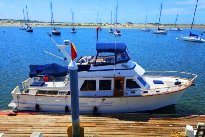 1983 Ocean Alexander 43 yacht docked in a scenic marina with sailboats in the background.