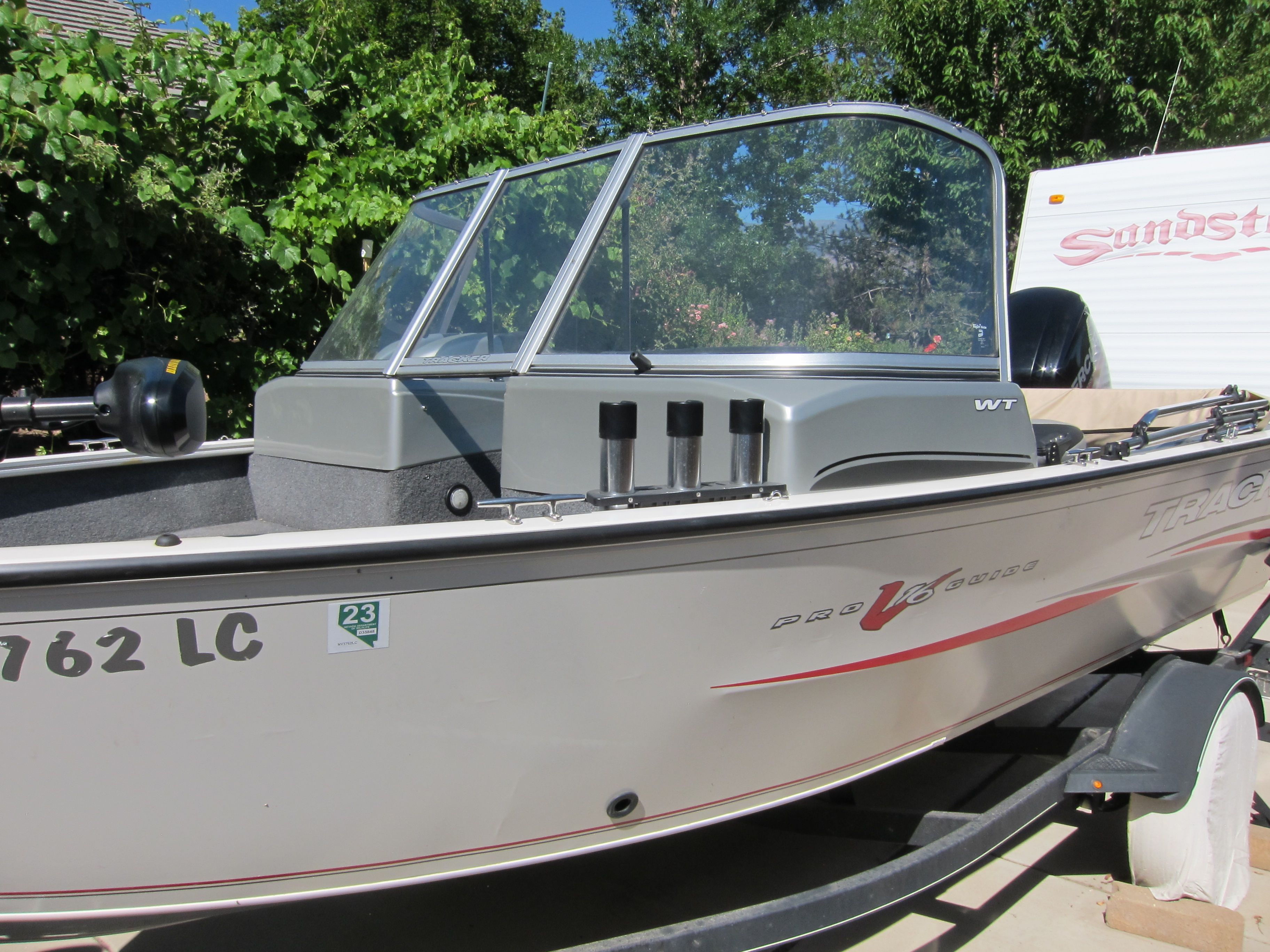 A 2018 Tracker Pro Guide V-16 WT boat on a trailer, surrounded by trees and a camper.