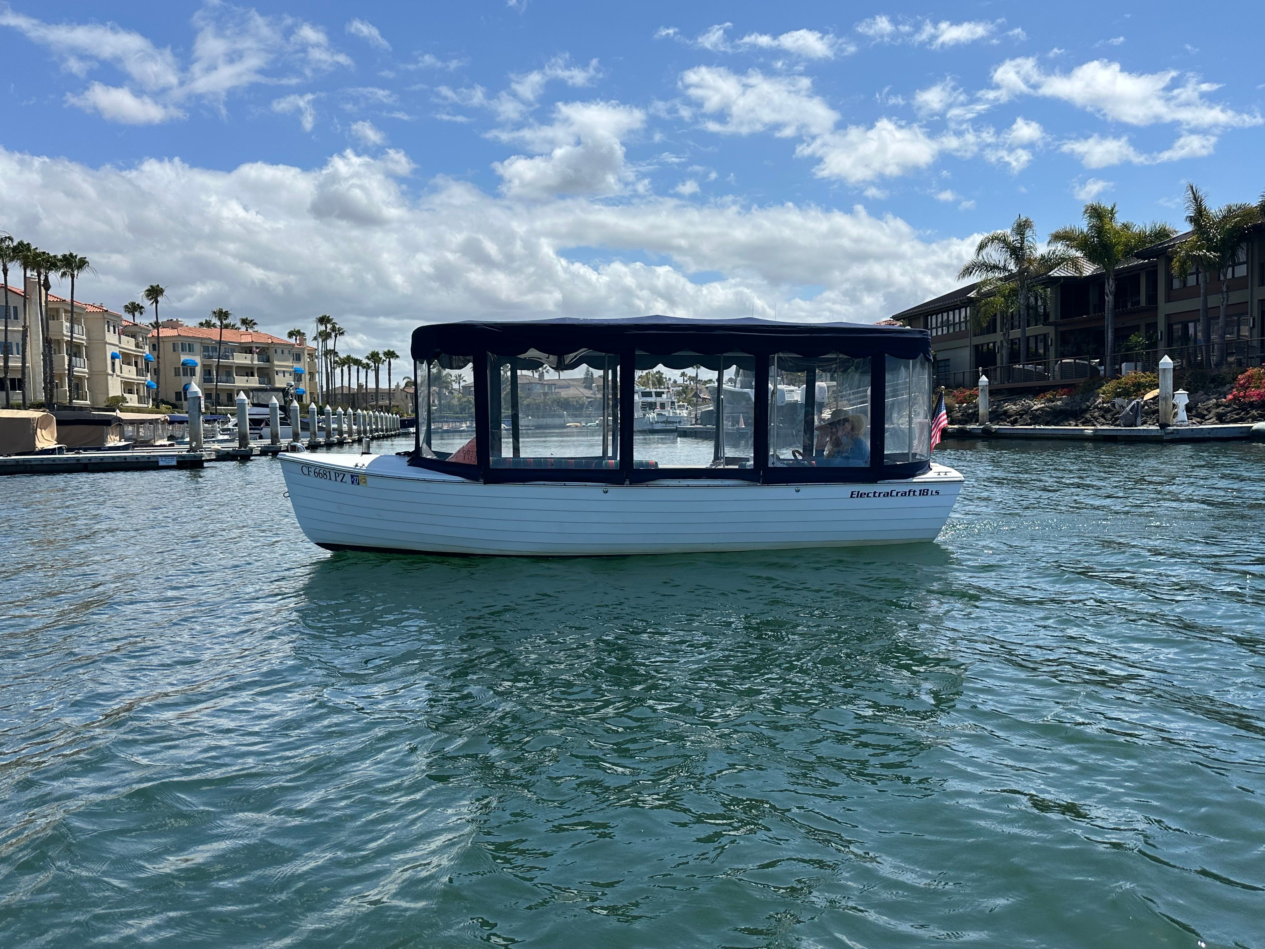 A white boat with a black canopy is on calm water in a harbor.