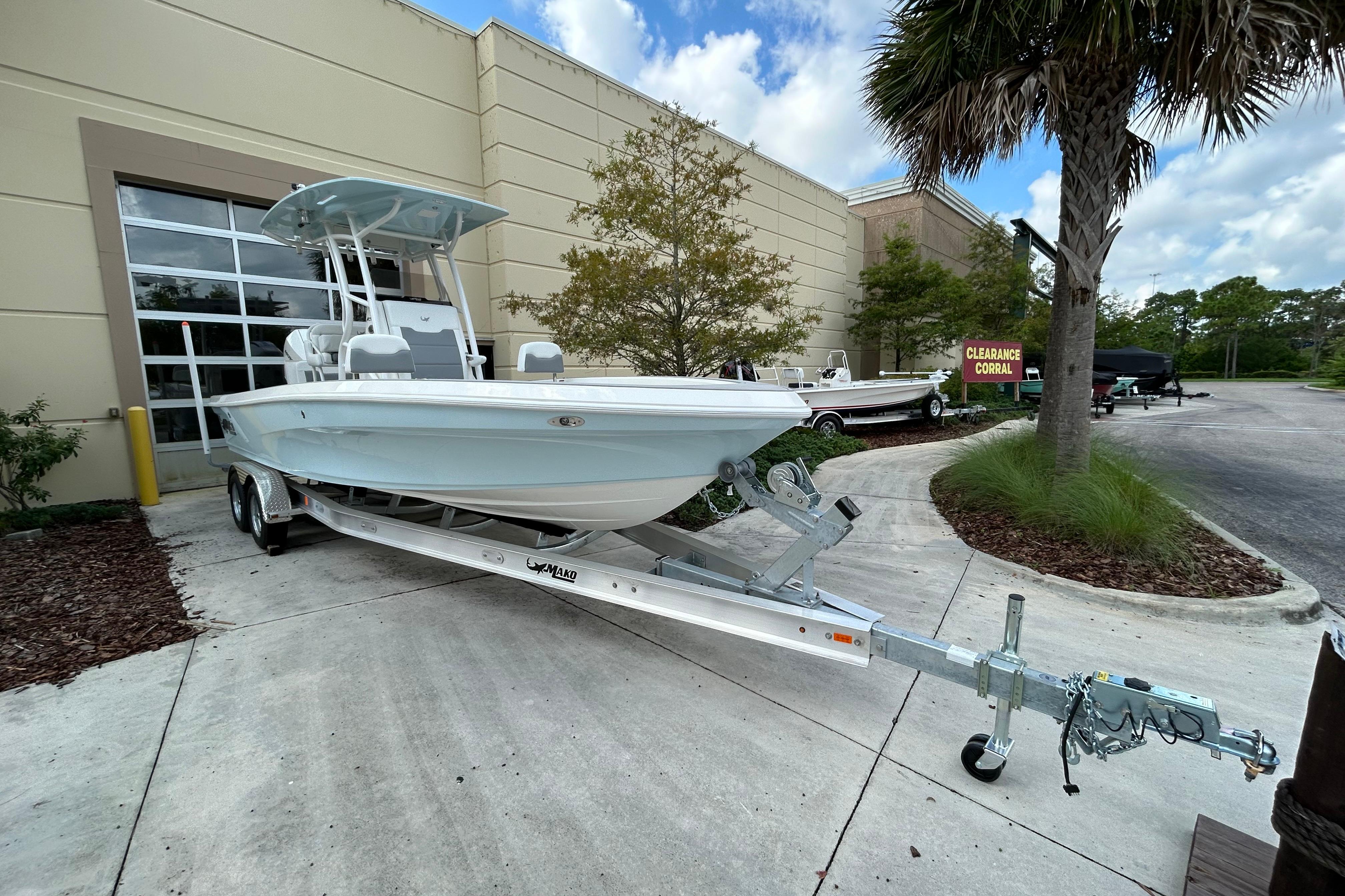 2025 Mako 24 APEX boat on trailer outside dealership, clear sky, palm tree nearby.