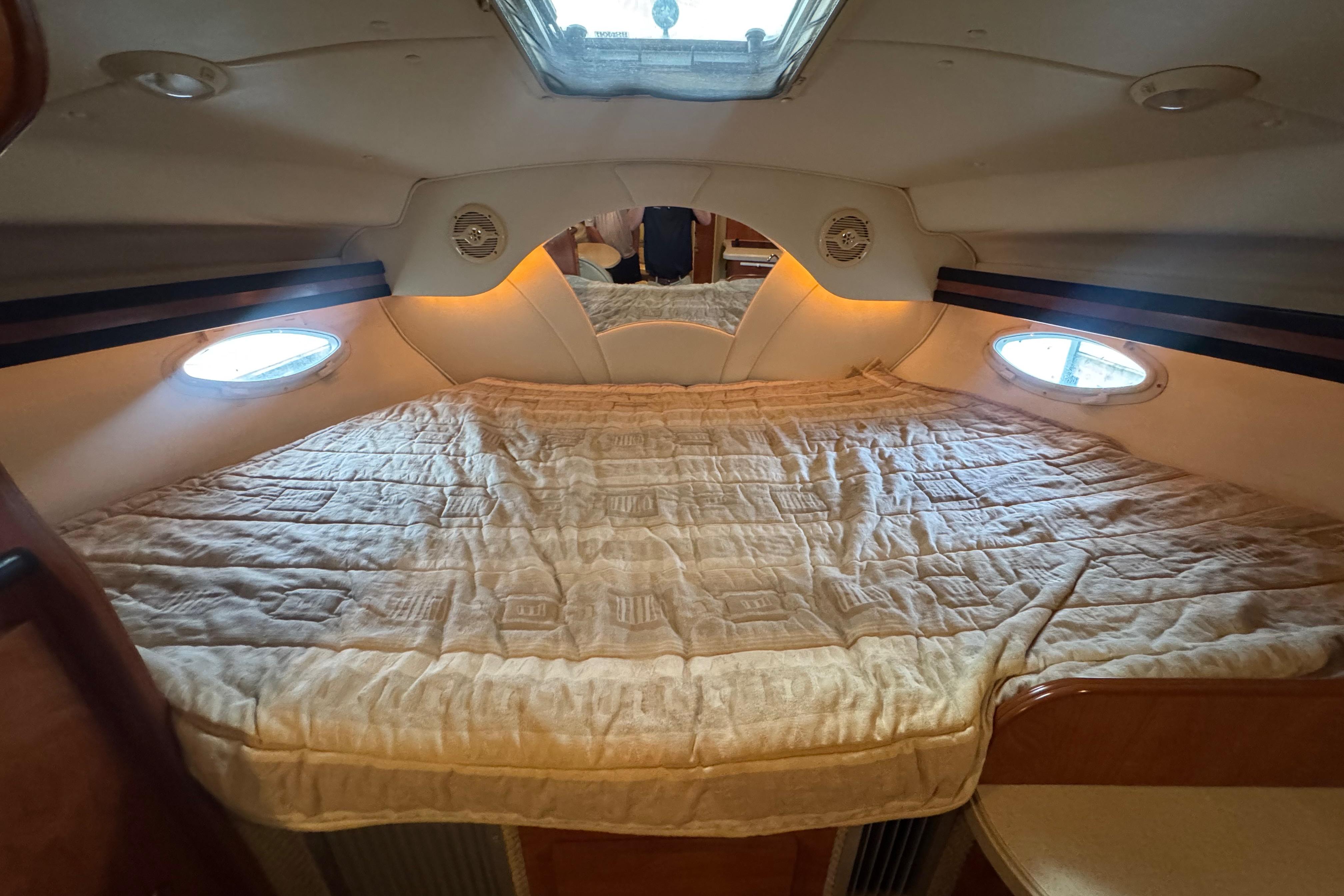 Interior cabin of 2004 Rinker Fiesta Vee 312 with cozy bed and porthole windows.