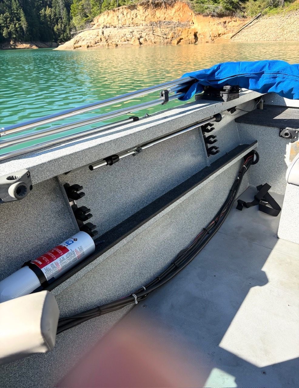 The image shows the interior of a boat with gray seating and a fire extinguisher. It's on calm water.