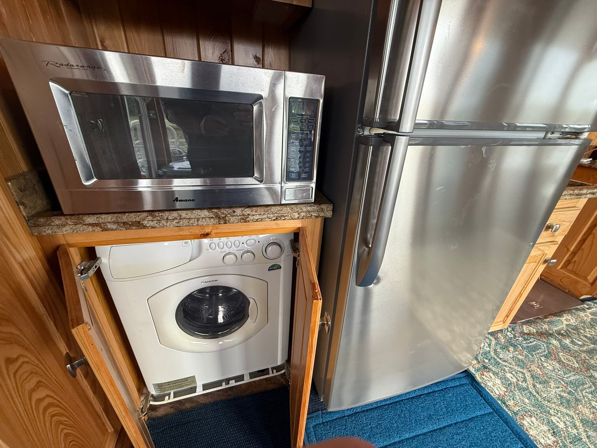 A kitchen with a microwave, refrigerator, and washing machine in a wooden cabinet.