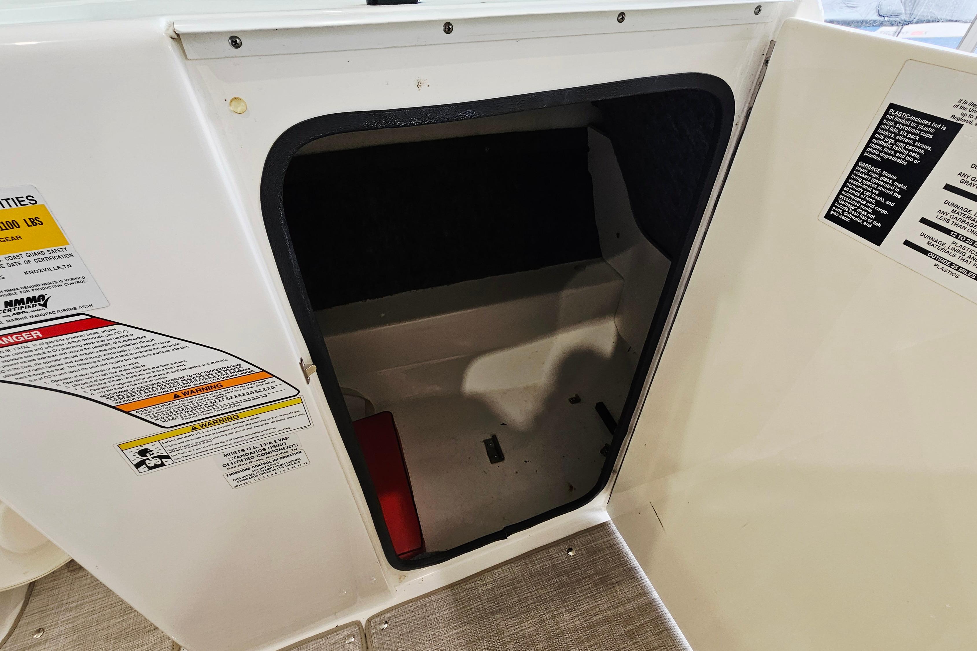 Storage compartment on a 2012 Sea Ray 200 Sundeck boat with safety labels.