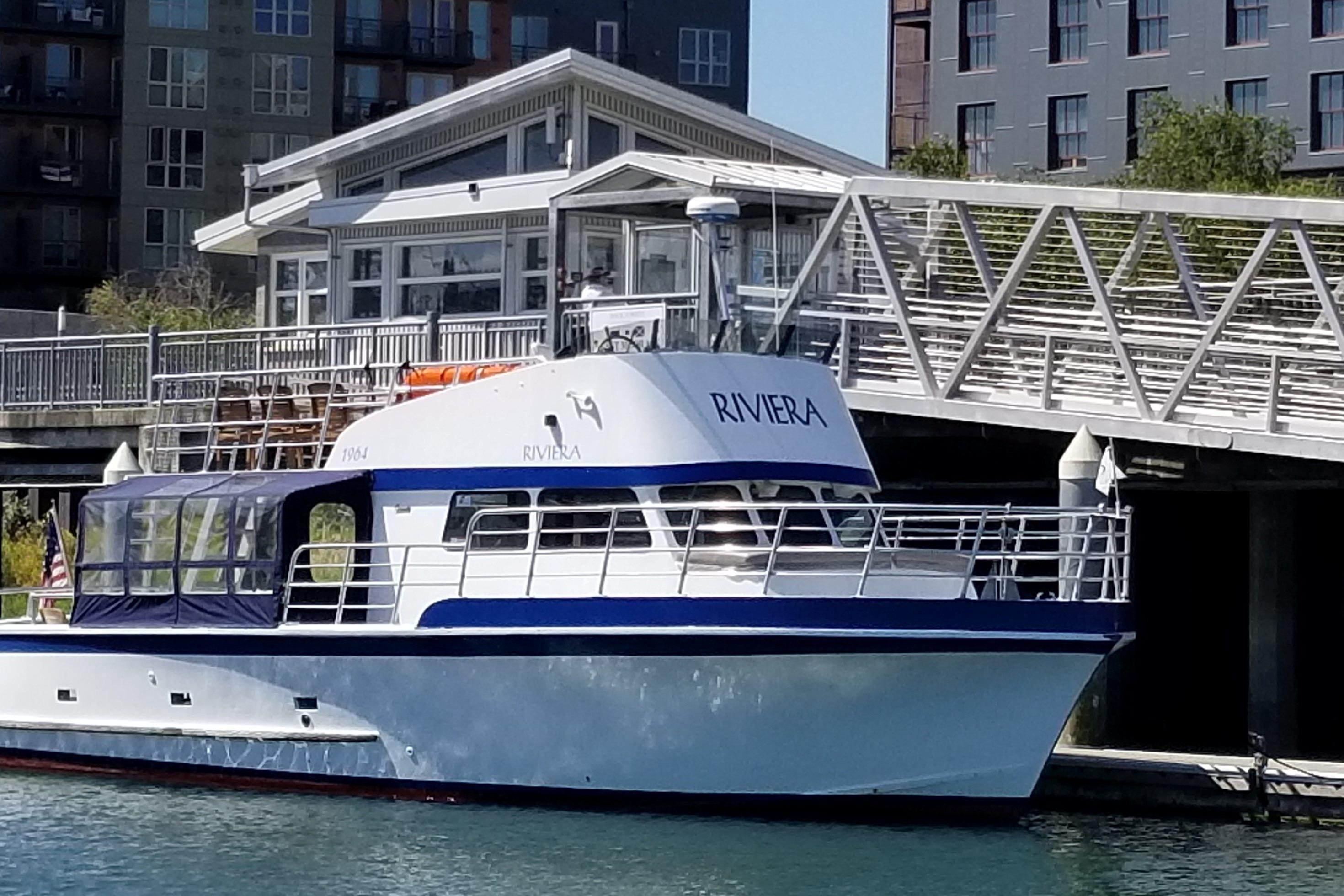 Vintage 1964 Grandy Tour Boat "Riviera" docked near modern waterfront buildings.