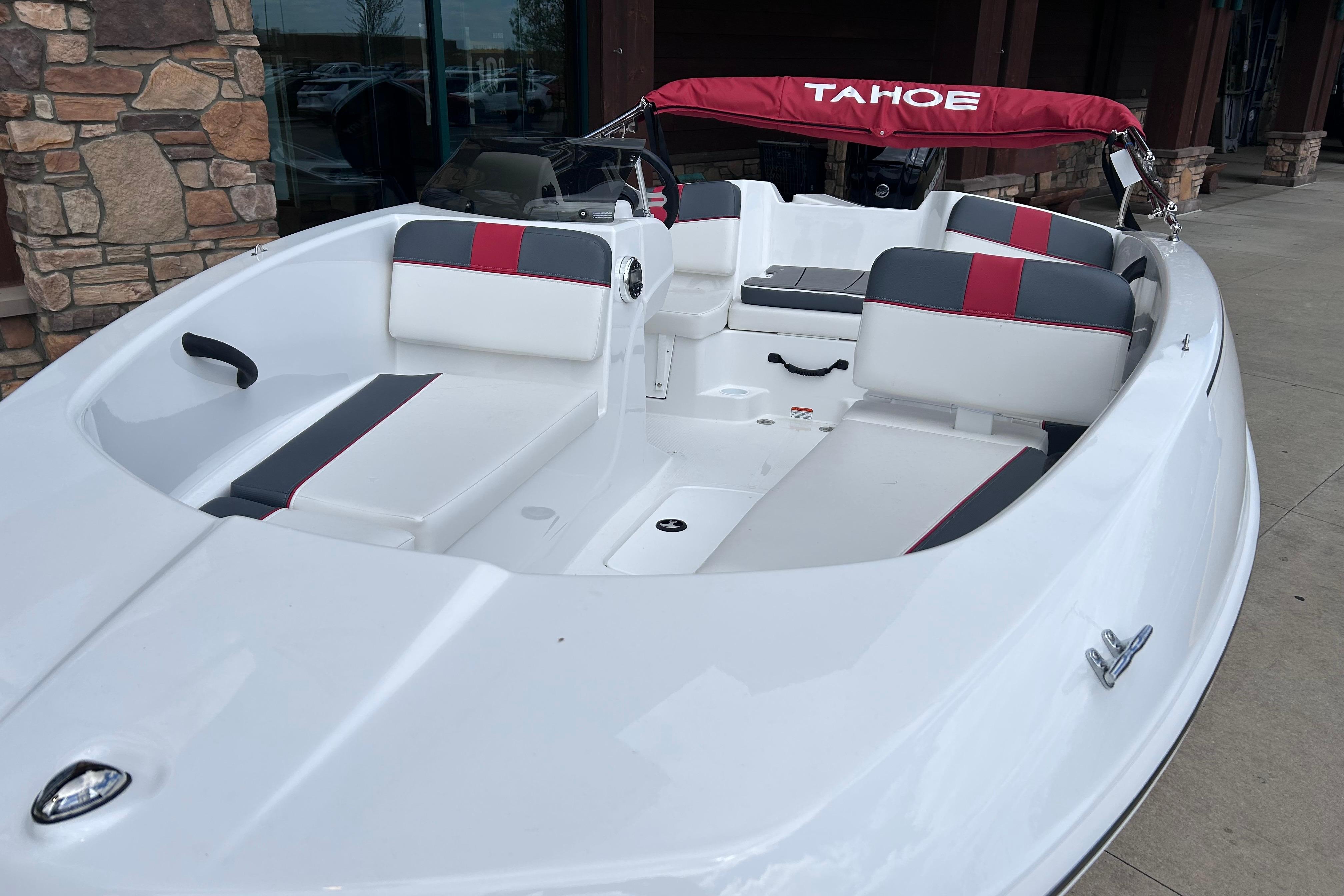 2026 Tahoe T16 boat with red and gray seating, docked near stone wall.