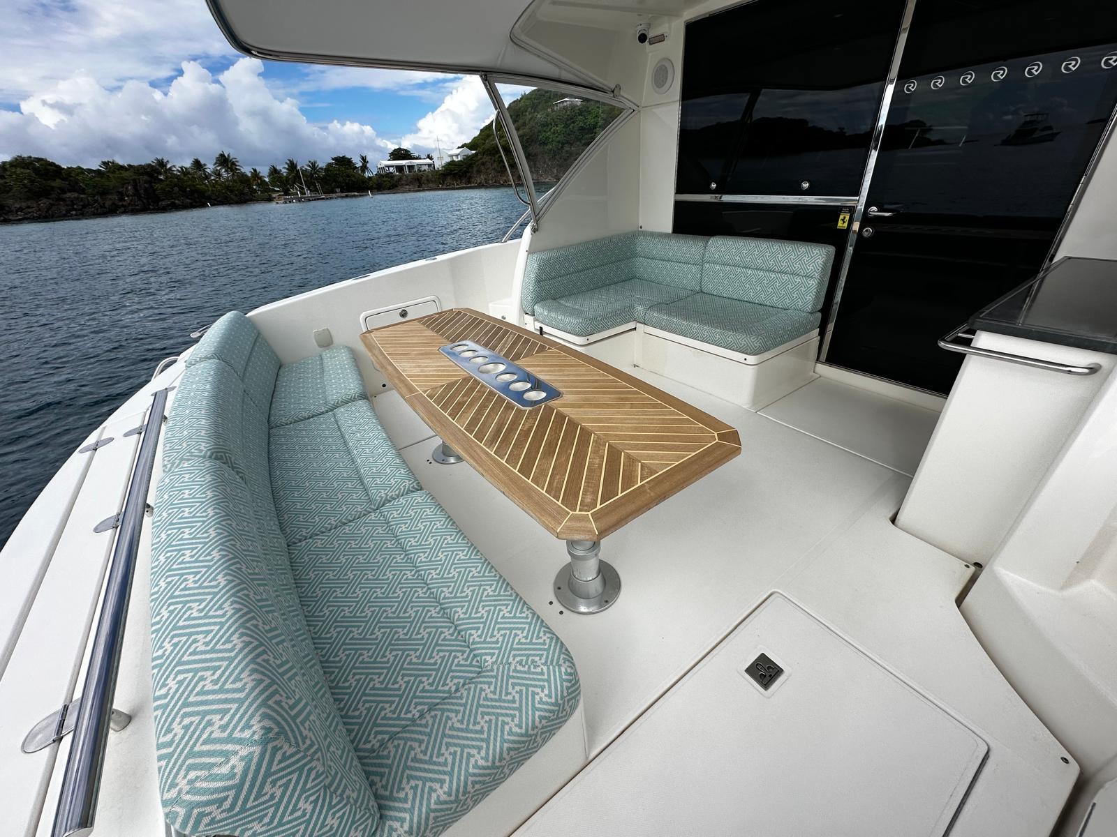 2016 Riviera 5000 Sport Yacht deck with cushioned seating and wooden table, overlooking serene waters.