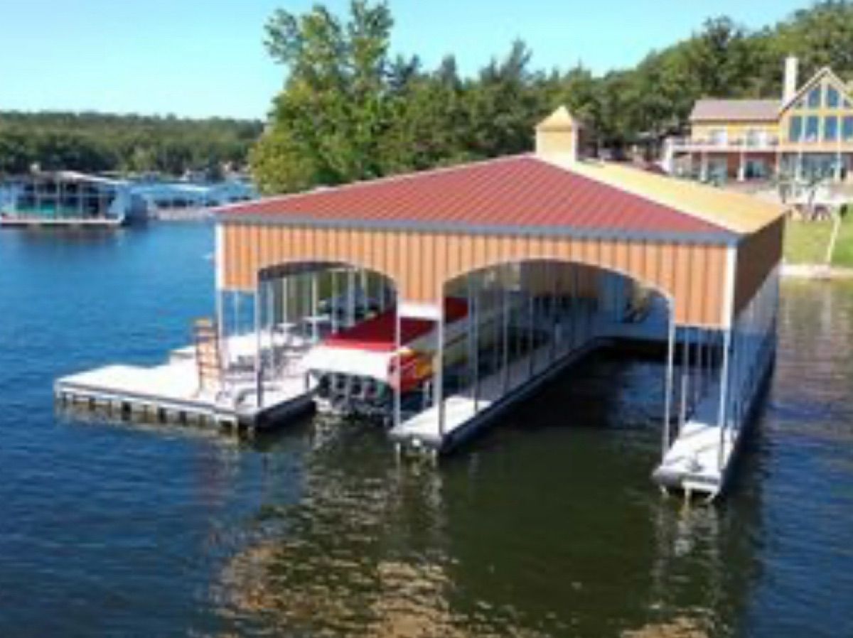 A boathouse with a red roof sits on a calm lake.
