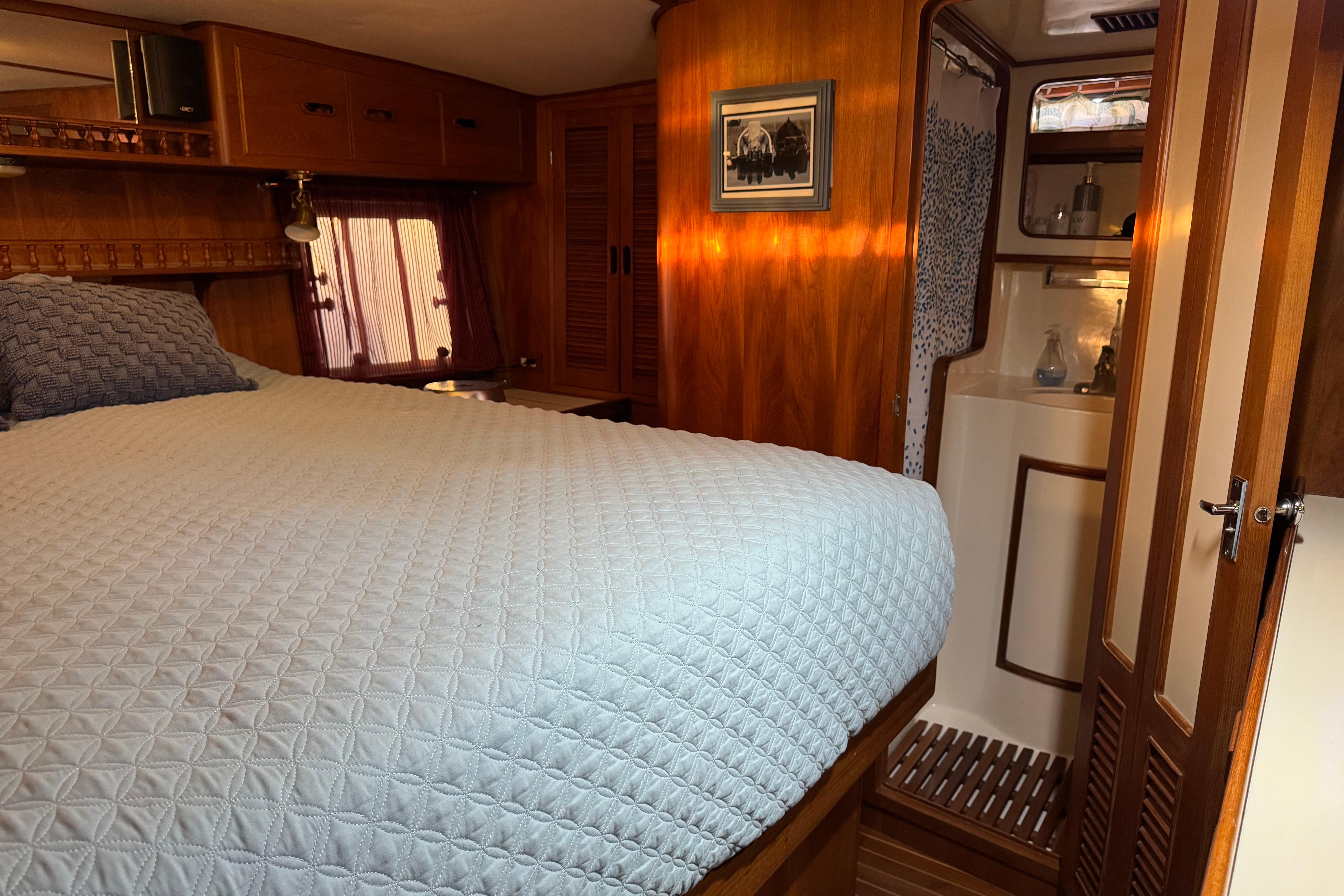 Cozy bedroom in 1987 President 37 yacht with wood paneling and ensuite bathroom.