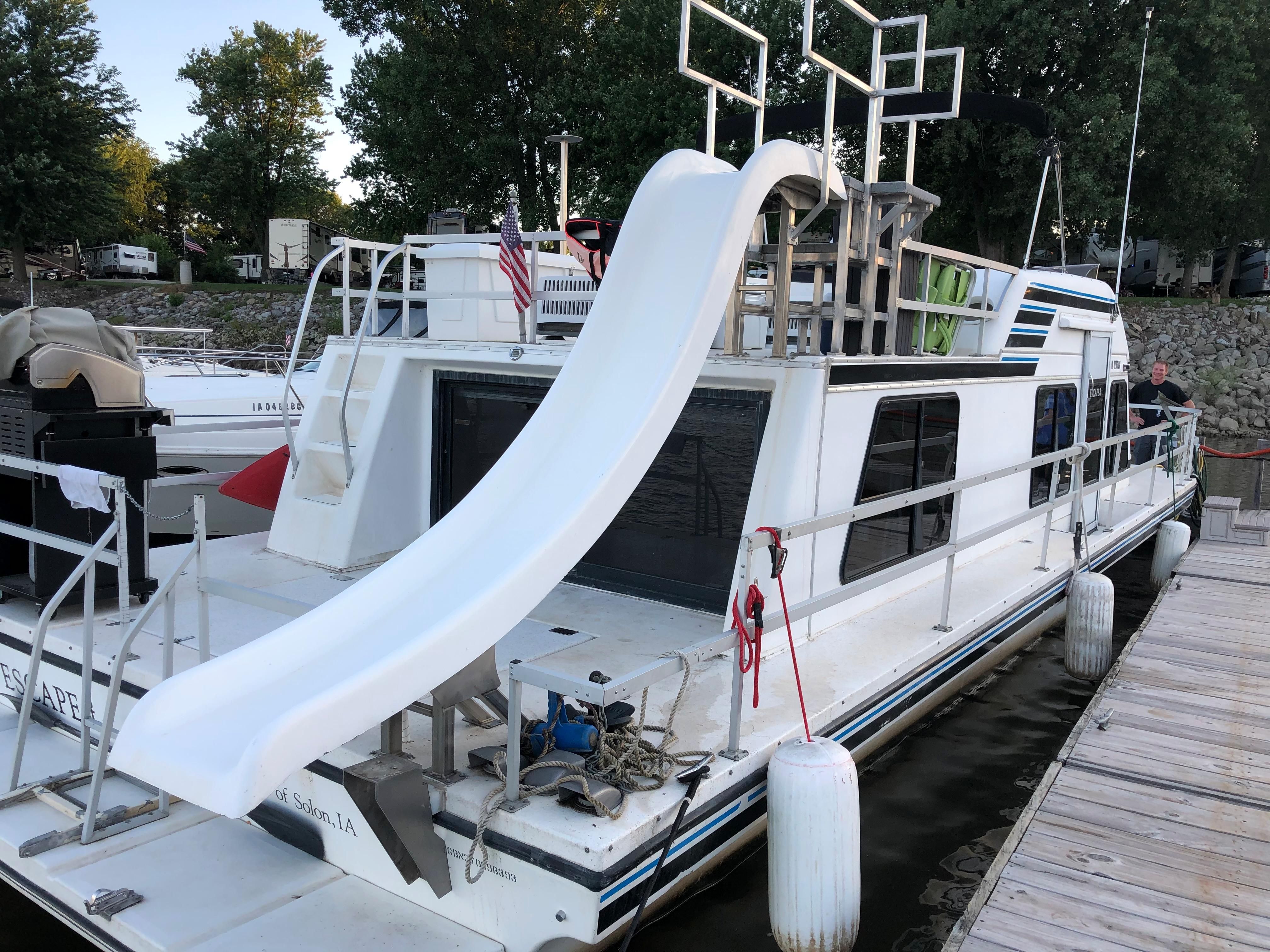 A 1993 Gibson Sport Series houseboat with a large waterslide at the stern, docked at a pier.