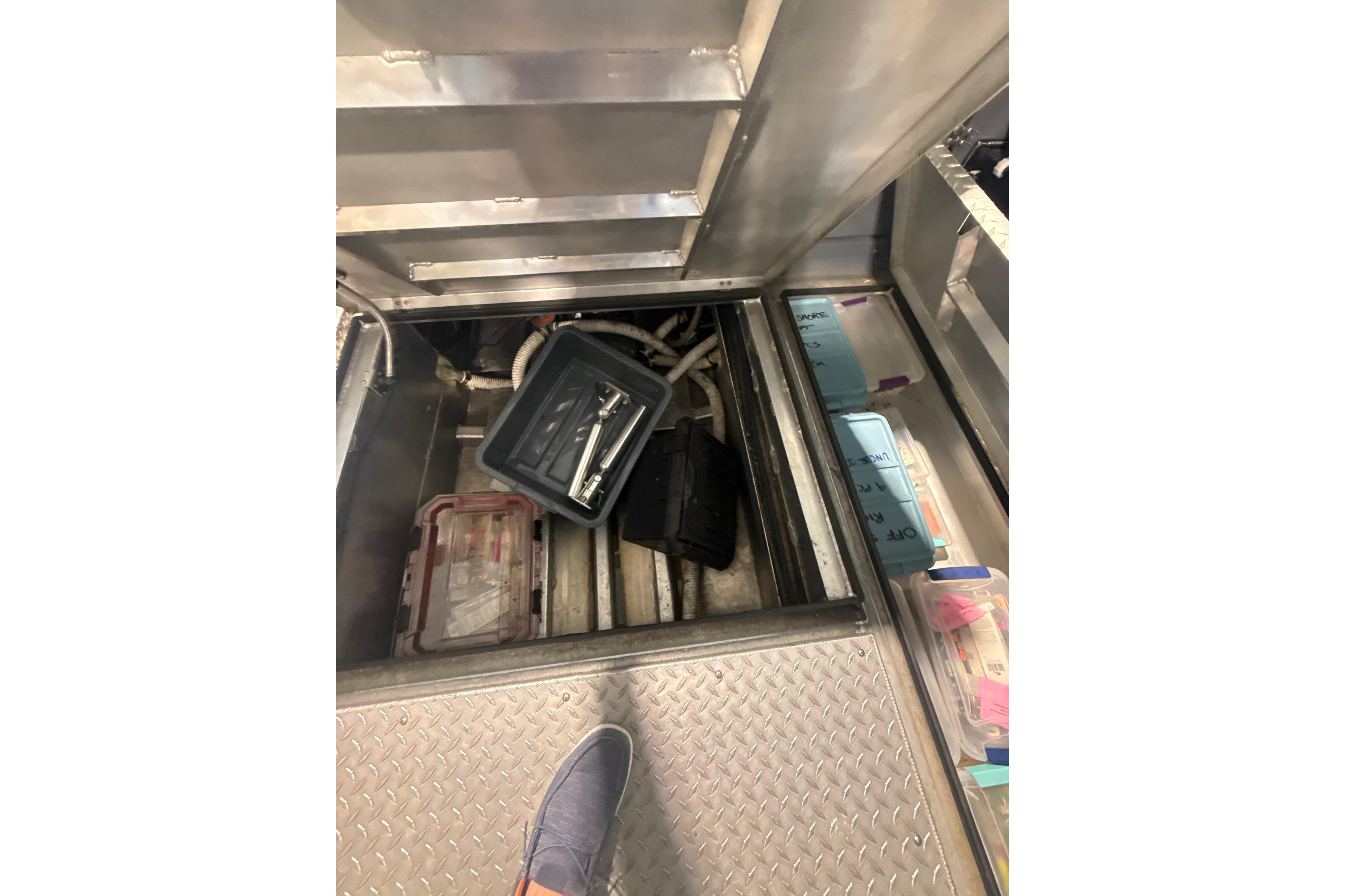 Interior storage compartment of 2022 Hewescraft 270 Alaskan Hardtop with tools and containers.