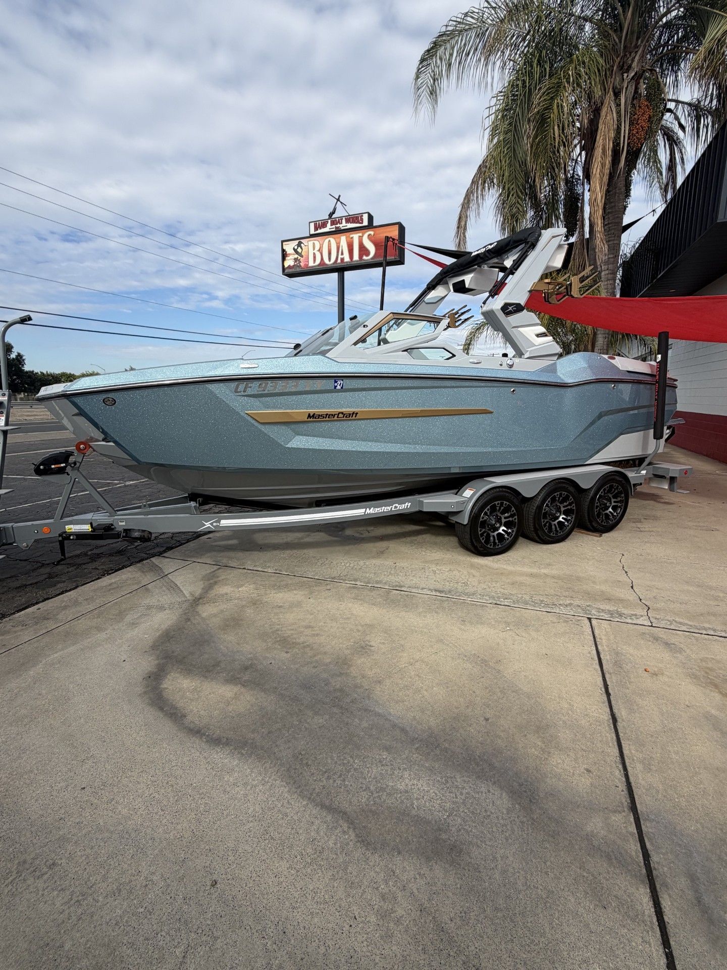 A MasterCraft X24 boat on a trailer, parked on a sidewalk next to palm trees.