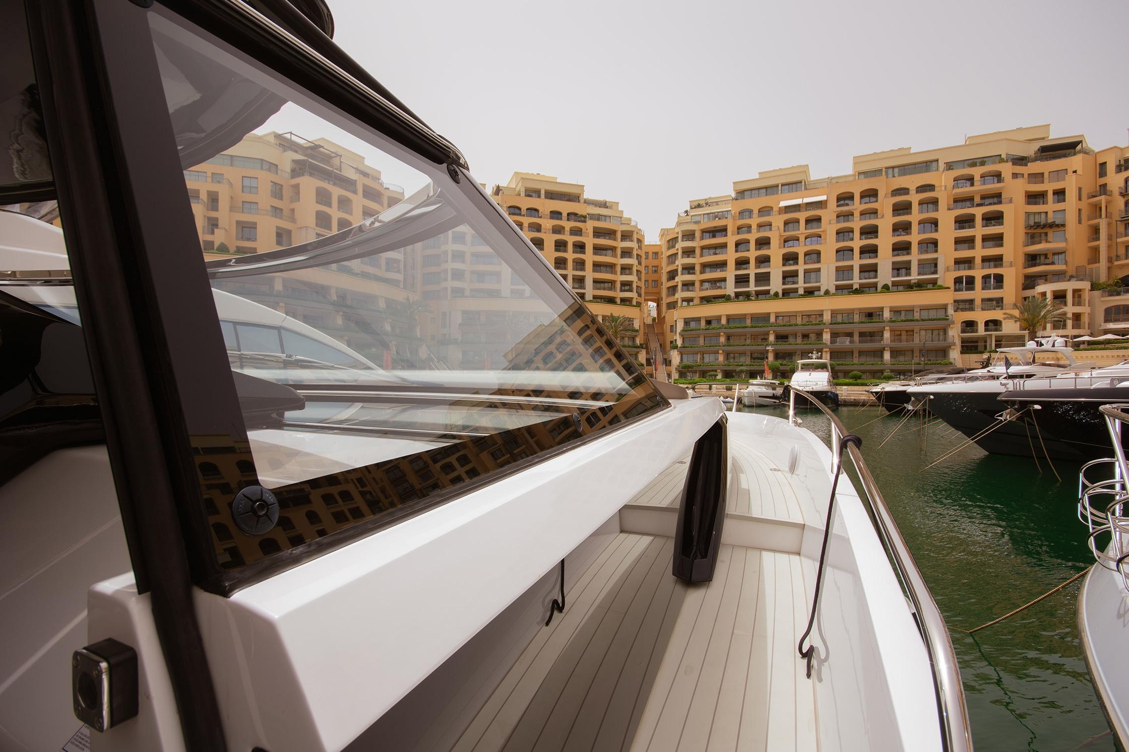 2024 Sunseeker Superhawk 55 yacht docked in a marina with luxury buildings in the background.