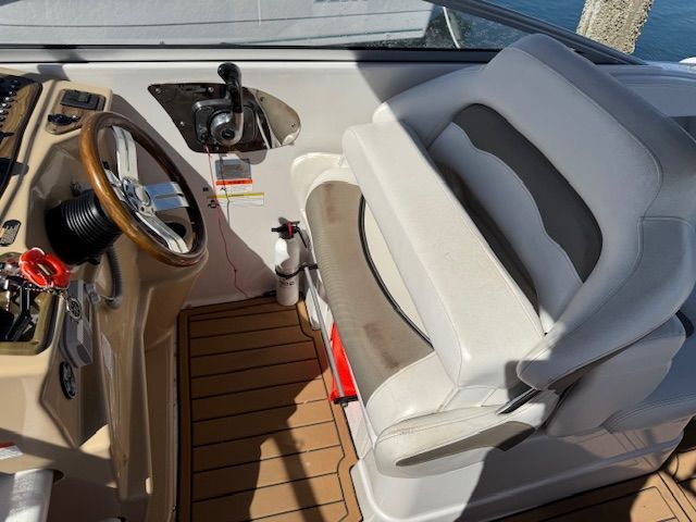 The image shows the cockpit of a Glastron GS boat with a white seat and wooden steering wheel.