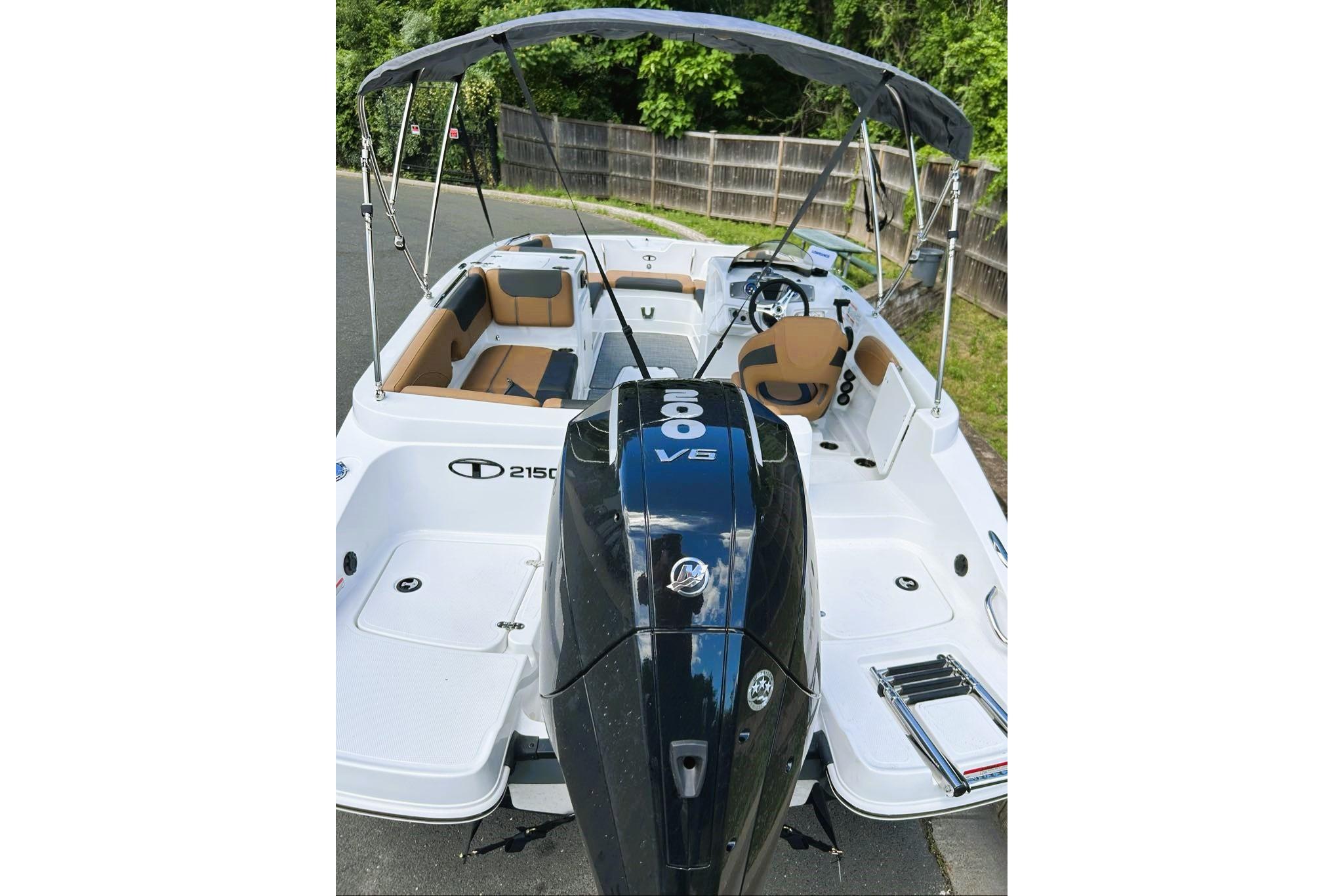 2026 Tahoe 2150 boat with outboard motor and canopy, parked on pavement.