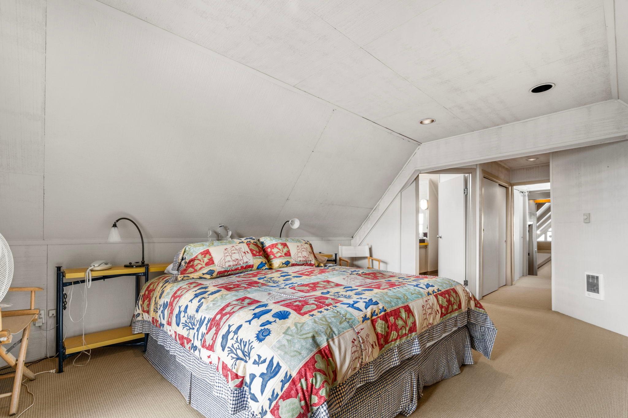 Cozy bedroom in a 1976 custom boathouse with colorful quilt and sloped ceiling.