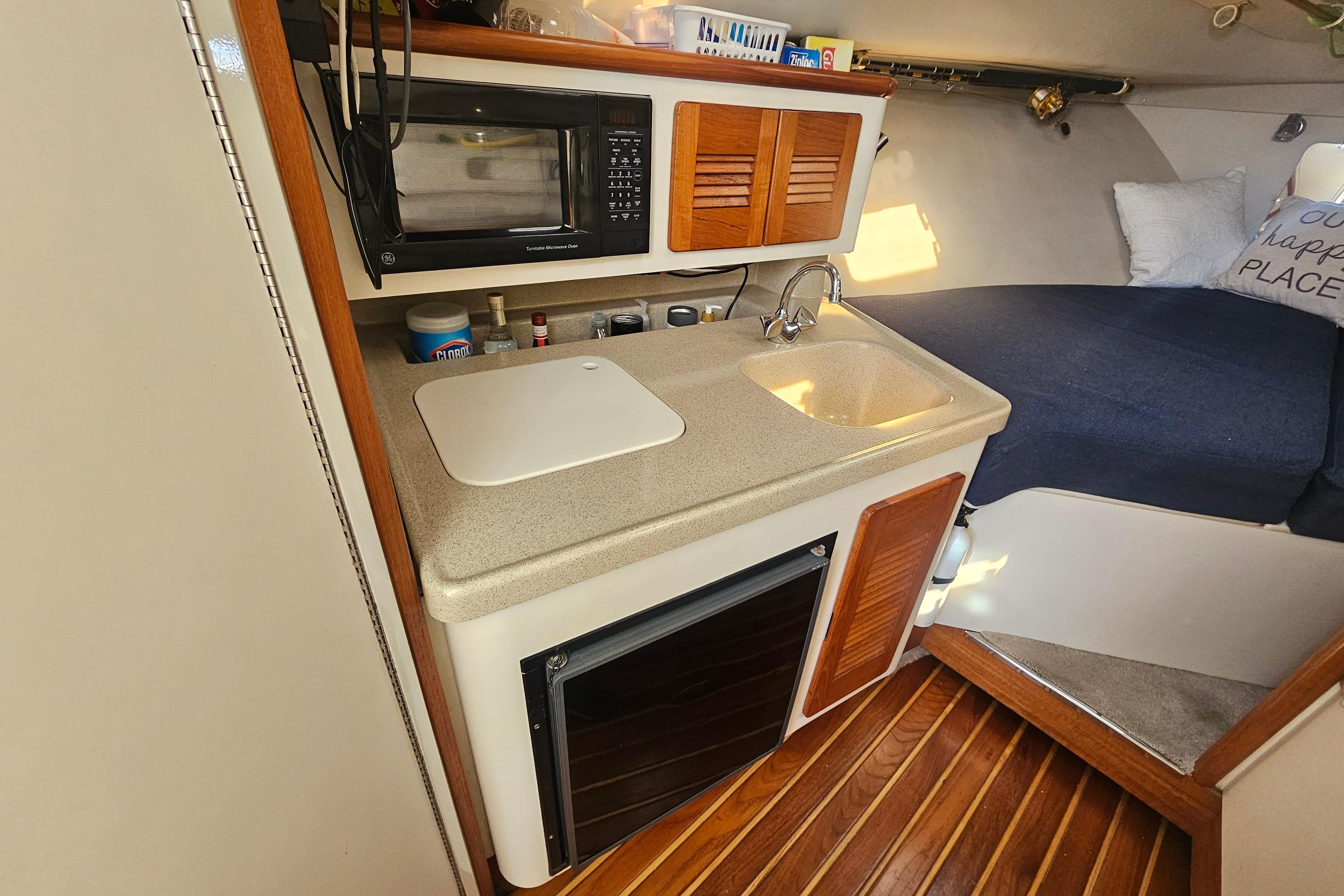 Compact kitchen area in a 2001 Pursuit 3000 Express boat with sink and microwave.