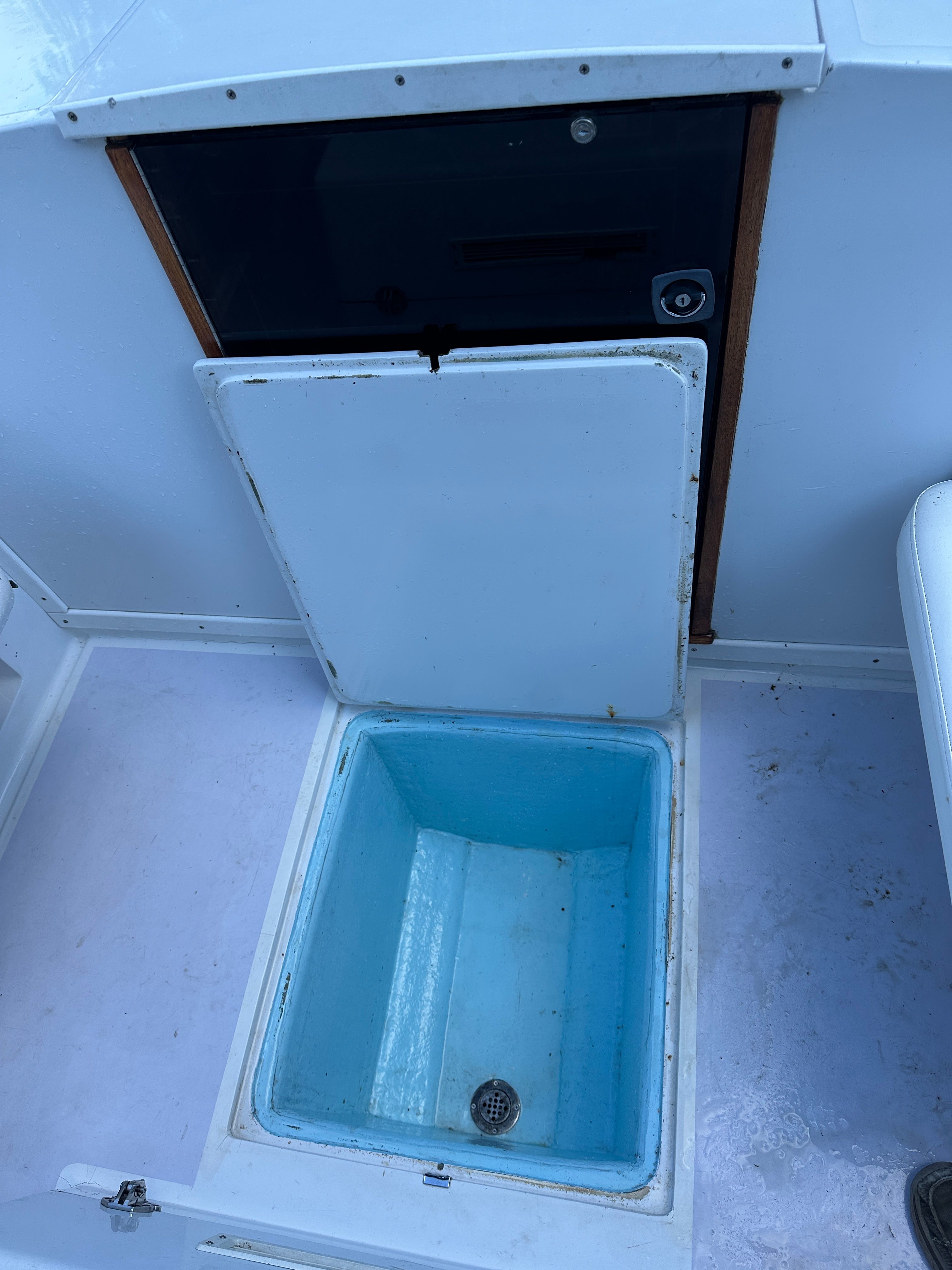 An open storage compartment on a boat with a blue interior and drain.