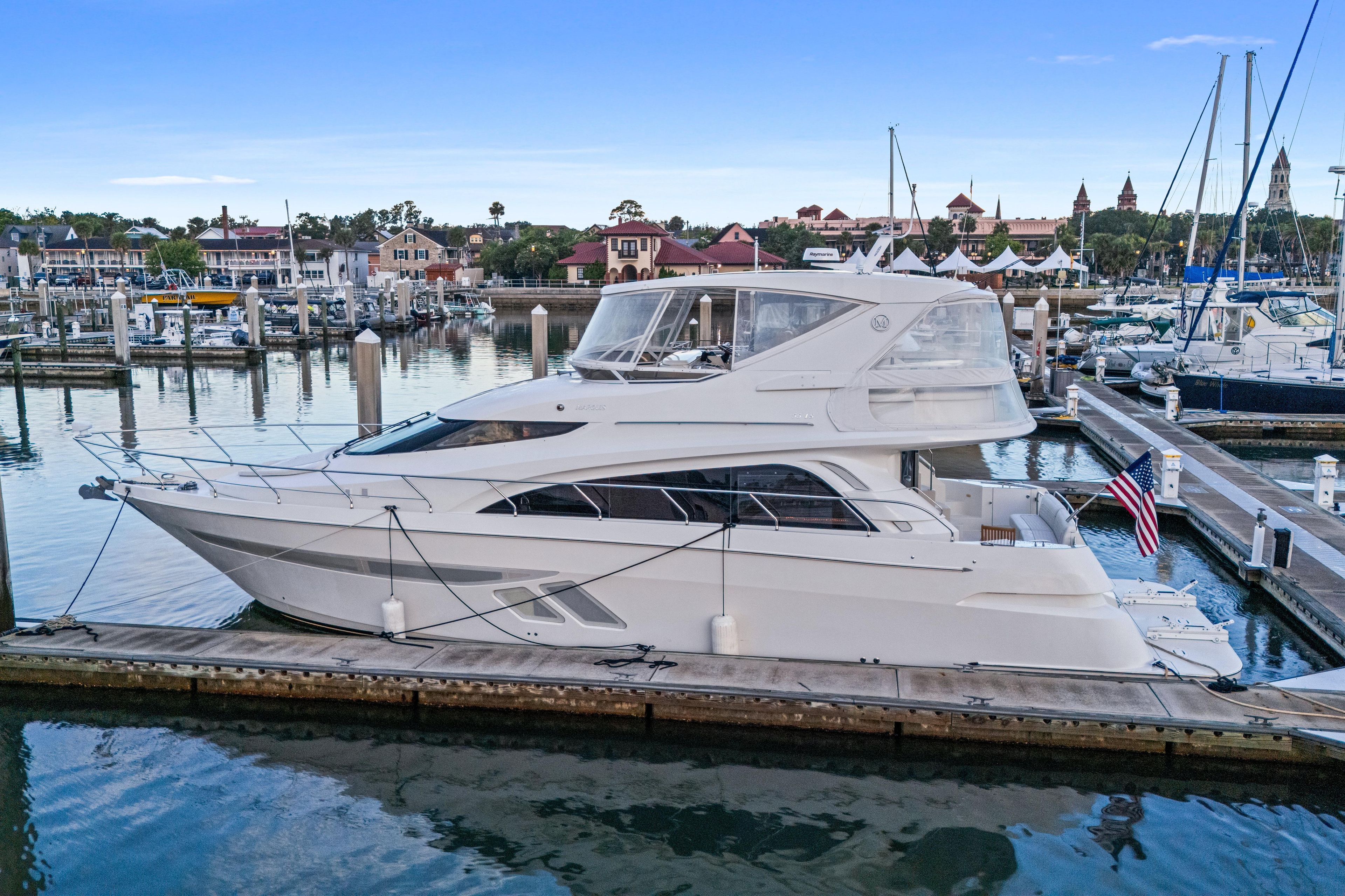 2007 Marquis 55 LS yacht docked in a marina, surrounded by calm waters and scenic buildings.