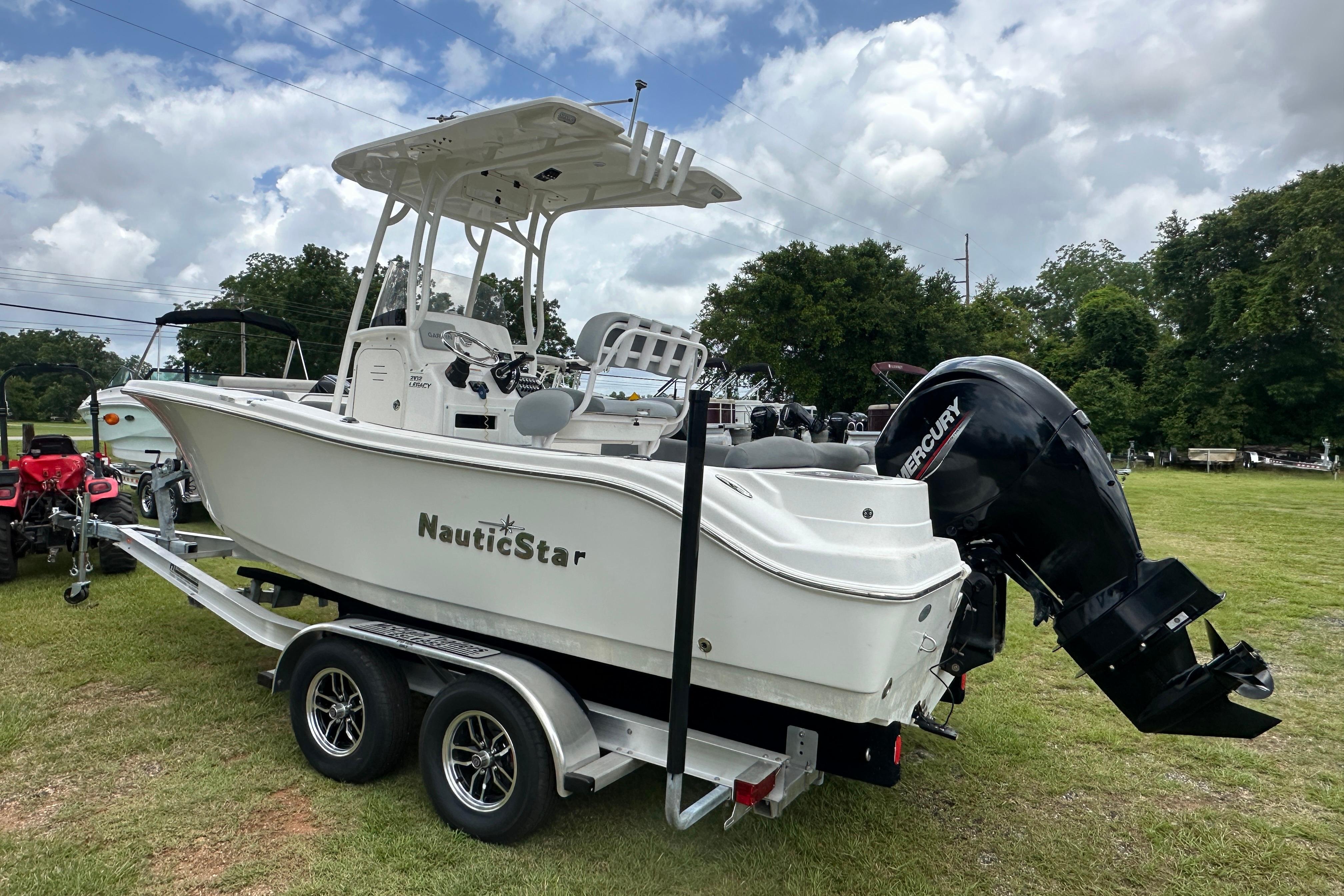 2023 NauticStar 2102 Legacy boat on trailer, featuring Mercury outboard motor, parked on grass.