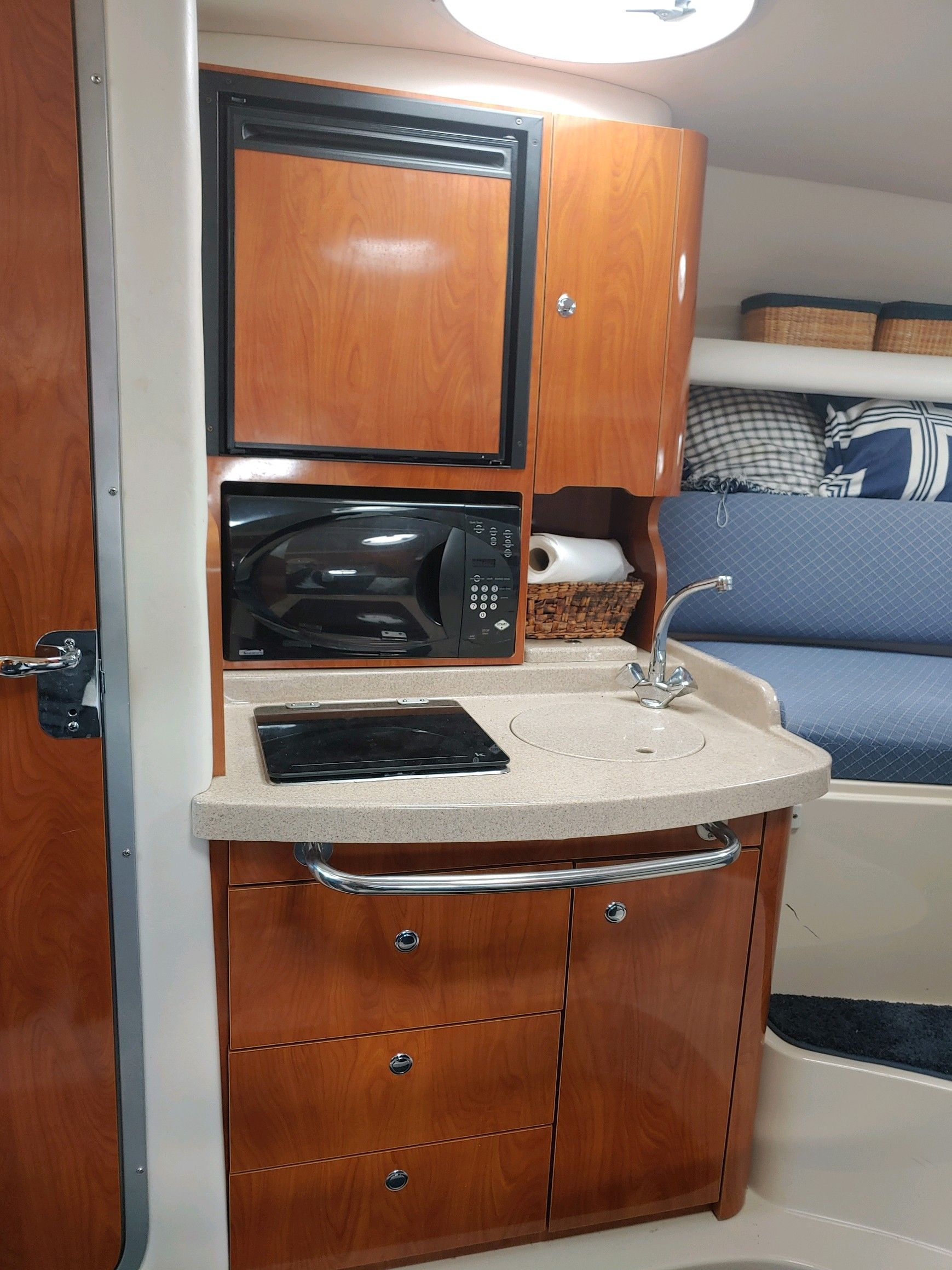 Compact boat kitchen with wooden cabinets, microwave, and sink, next to a cushioned bench.
