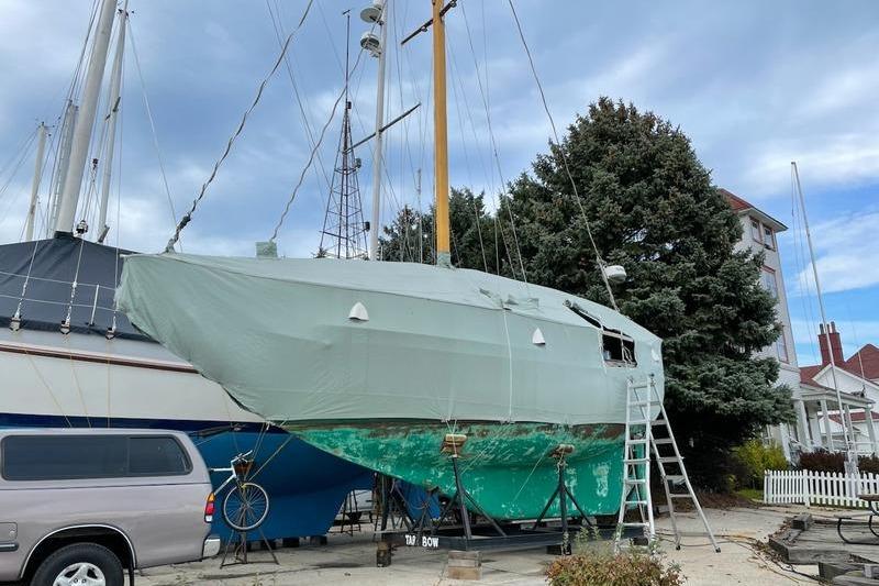 1980 Ta Shing Baba 30 sailboat on land, covered, with ladder and trees nearby.