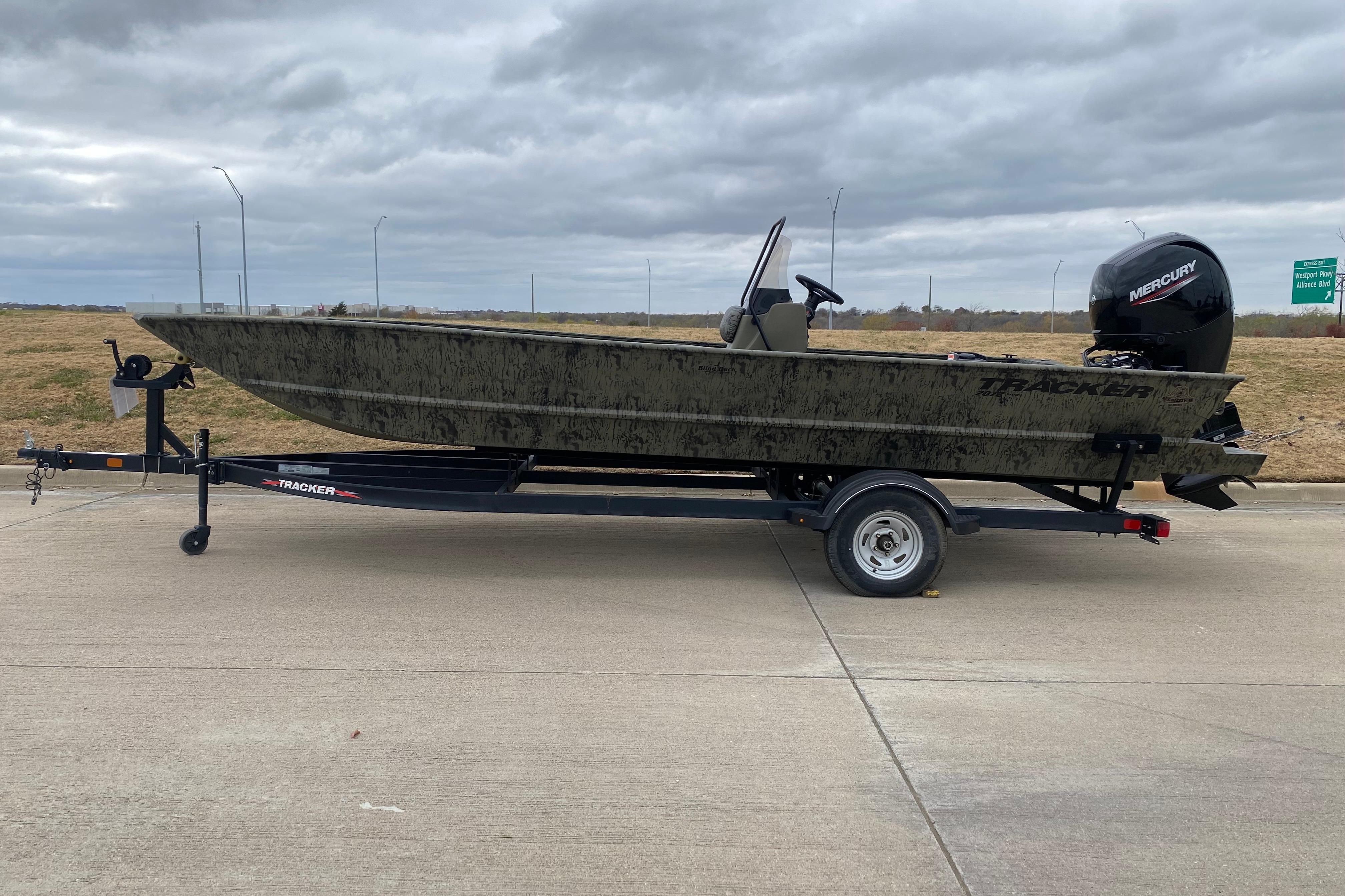 2026 Tracker Grizzly 2072 CC boat on trailer, parked on concrete under cloudy sky.
