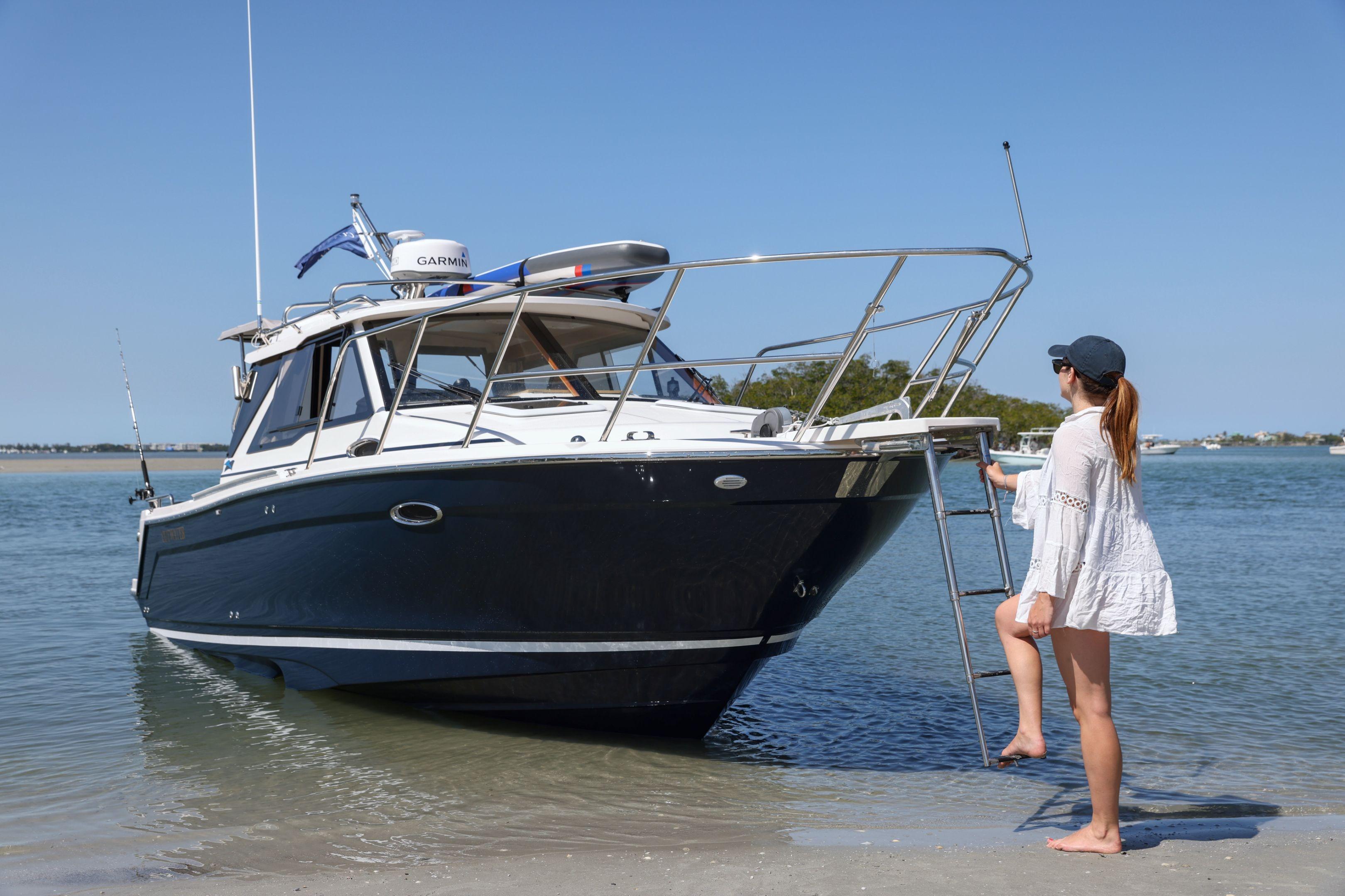 Woman boarding a 2026 Cutwater C-248 Coupe boat on a sunny beach.
