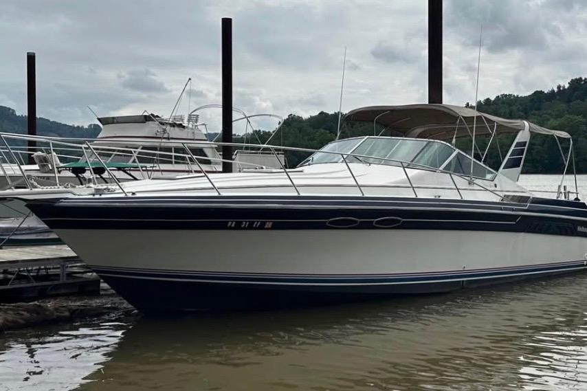 1987 Wellcraft 3400 Gran Sport boat docked on a calm river under cloudy skies.