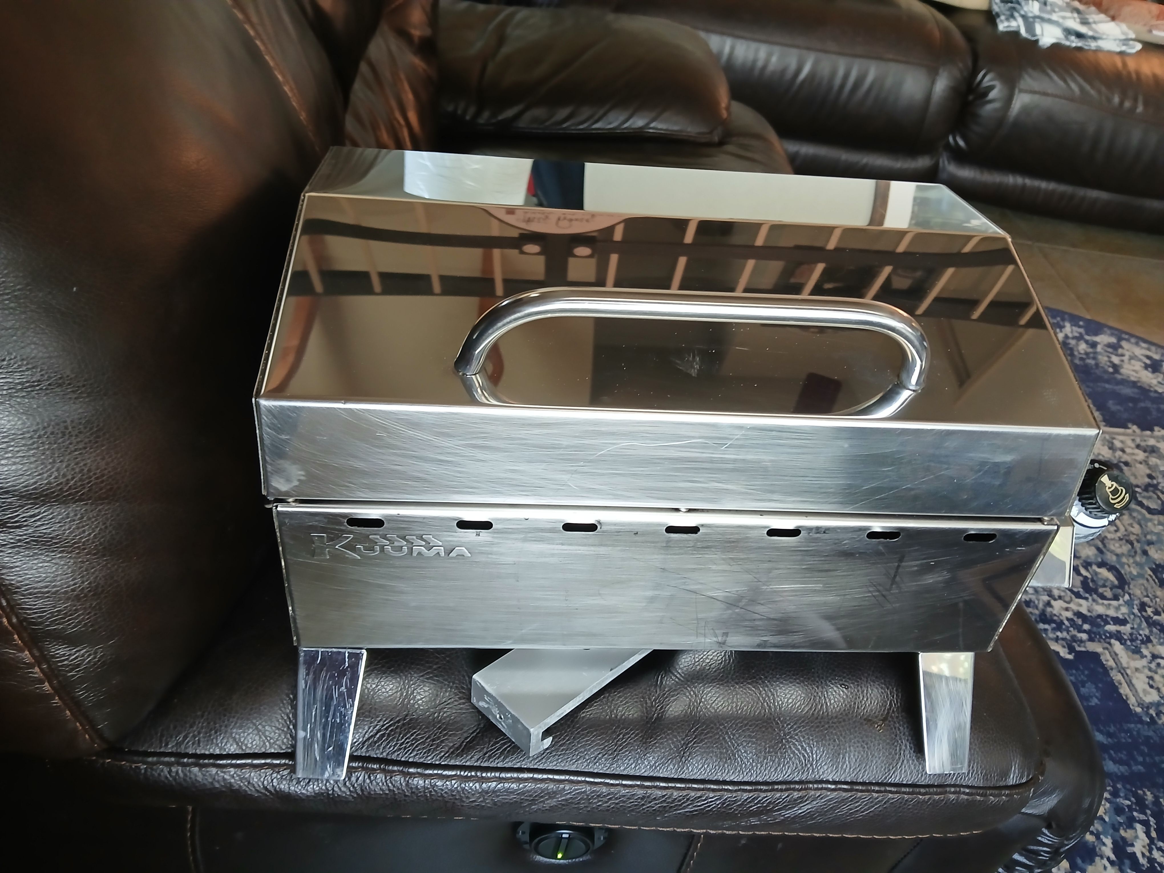 A portable stainless steel grill on a leather sofa.