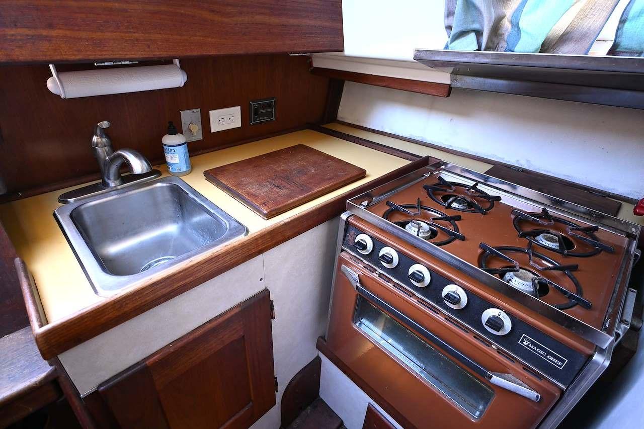 1977 Mercator Offshore boat kitchen with stove, sink, and wooden cabinetry.