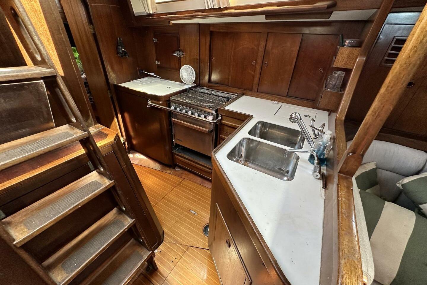 1988 Cambria 46 yacht interior kitchen with wooden cabinetry, stove, and dual sink.
