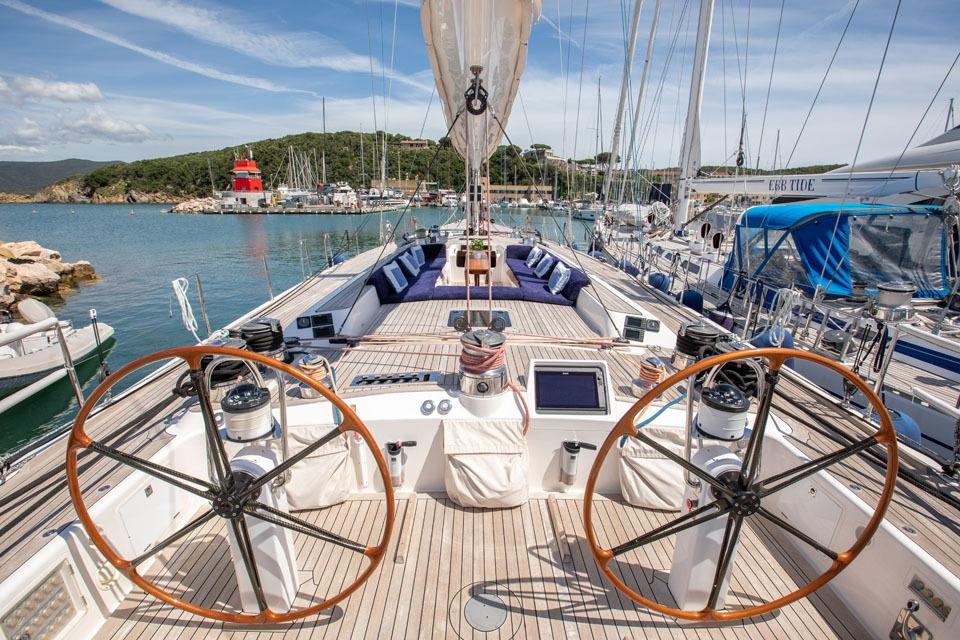 Luxurious 2001 Nautor Swan 80 yacht deck with dual steering wheels in a scenic marina.